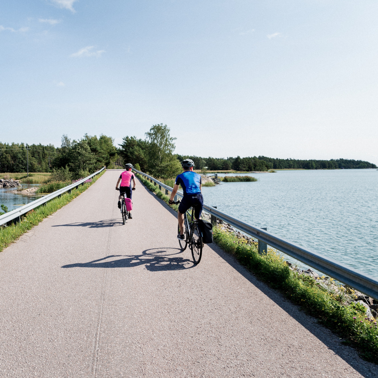 Two people crossing by bicycle a bridge overlooking a Finnish landscape.