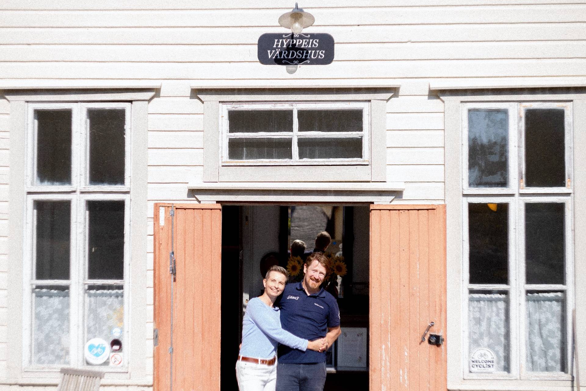 Hotel owners Outi and Sam hugging on the porch.