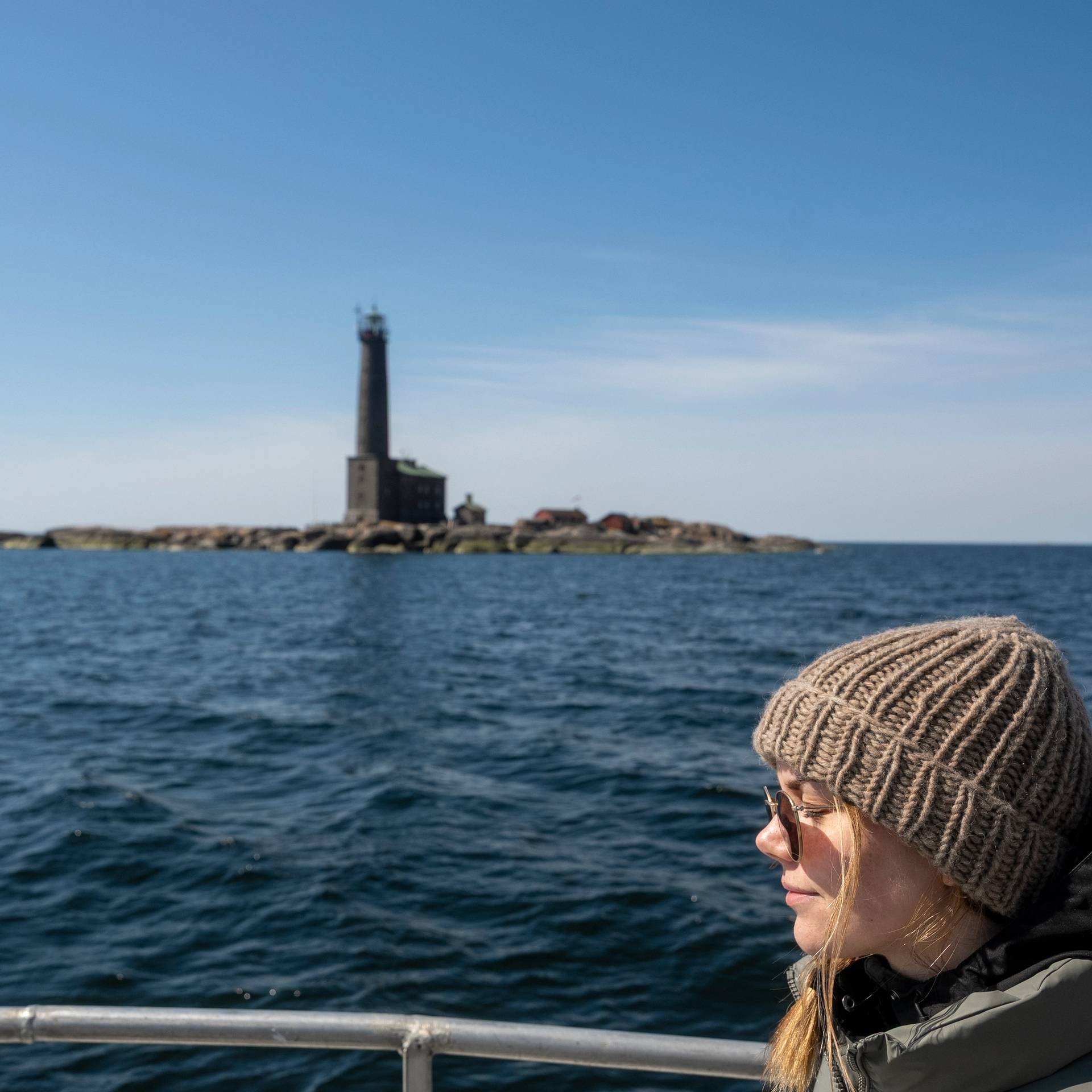 A girl on a boat with a lighthouse in the background.