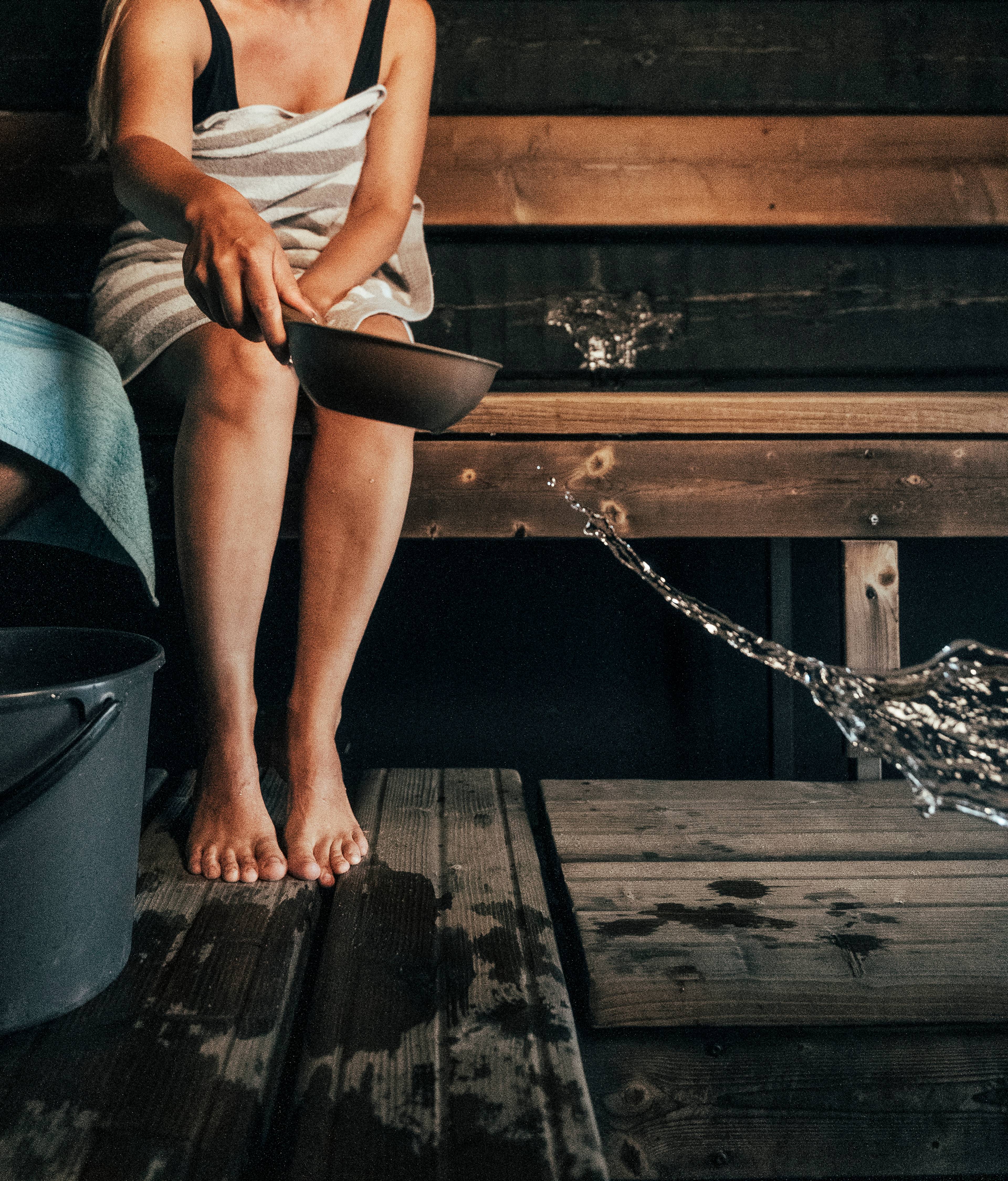 A person throwing water onto the sauna stove.