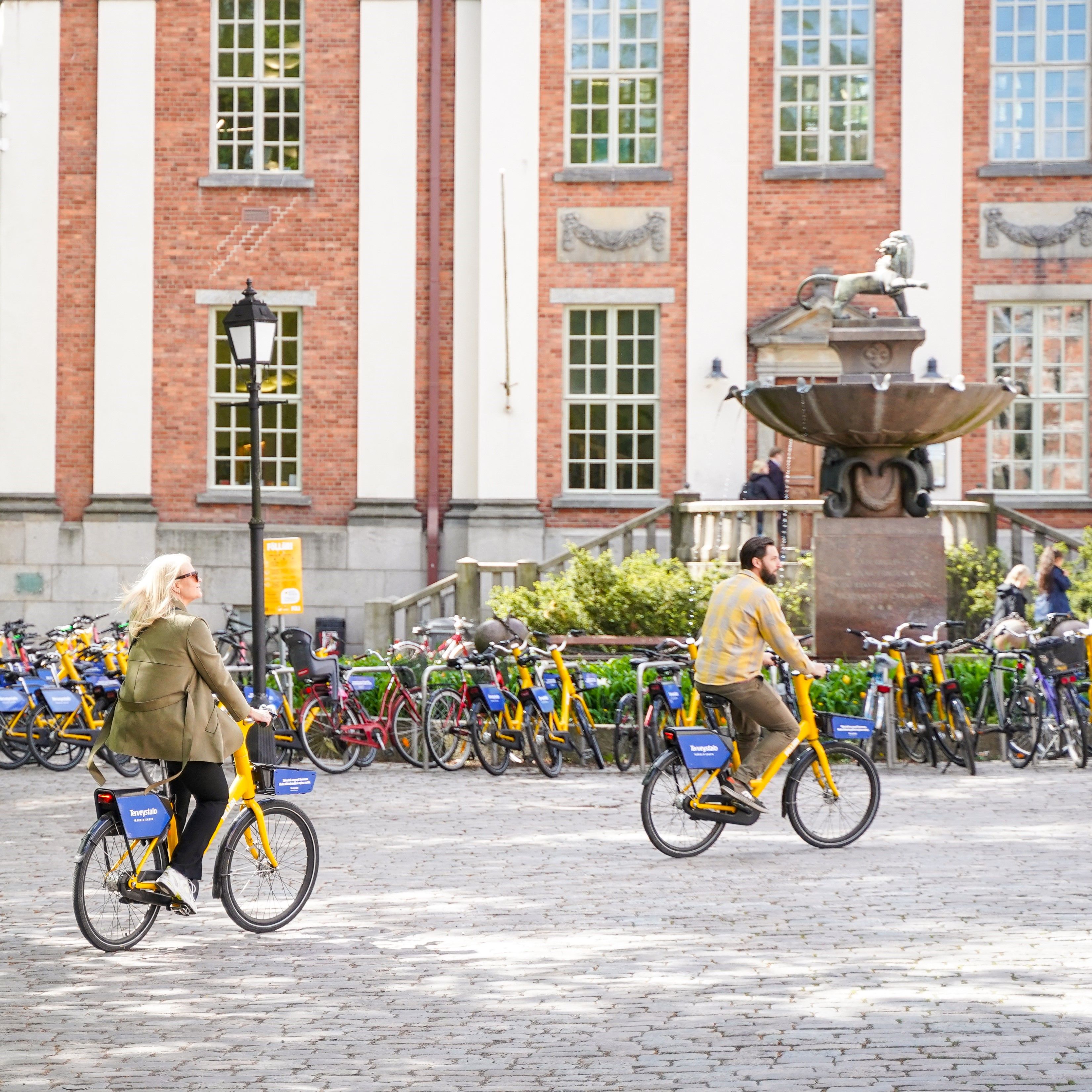 Two people riding city rental bikes on a sunny day