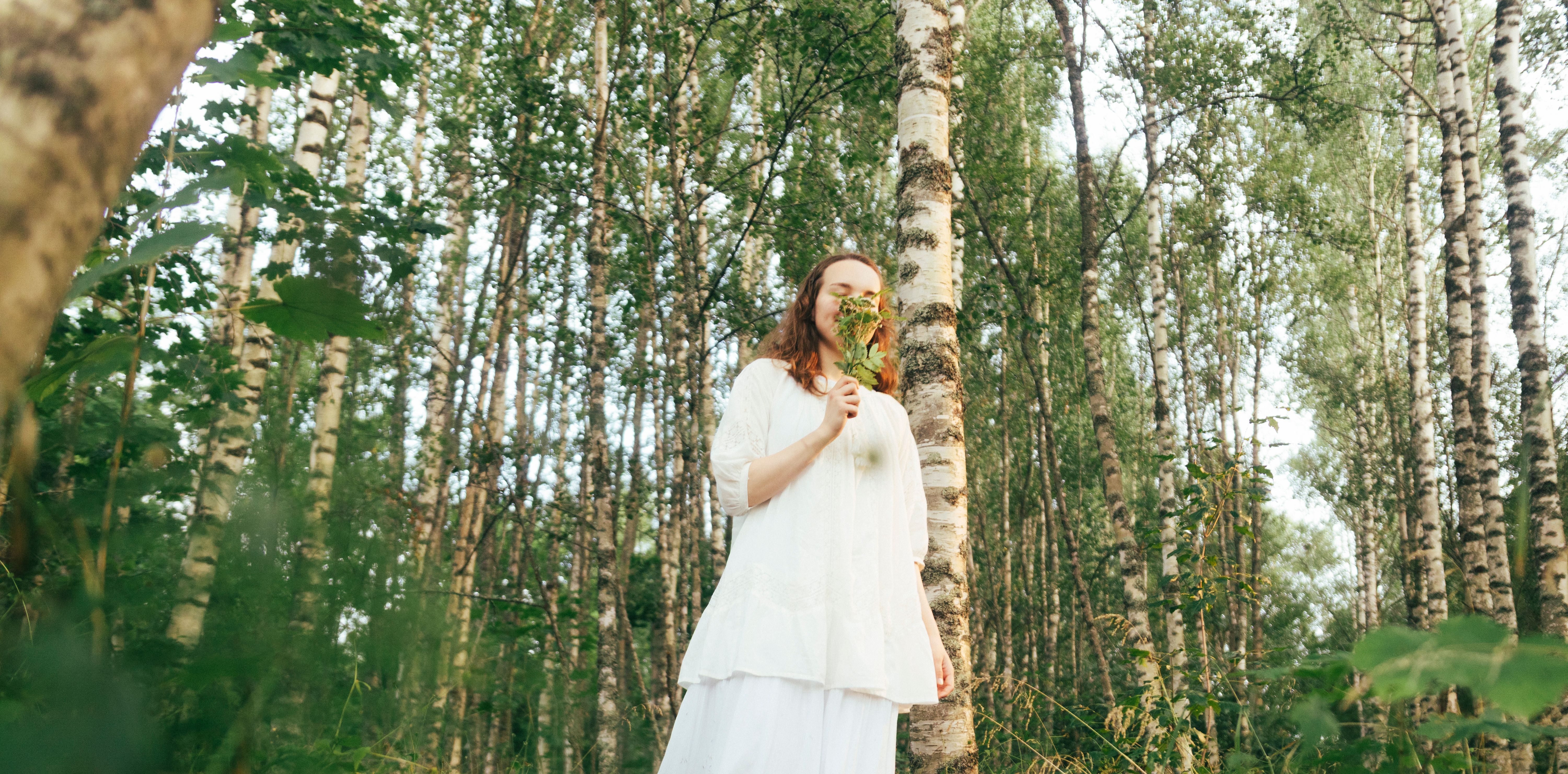 A girl smelling a budle of flowers in a birch forest.
