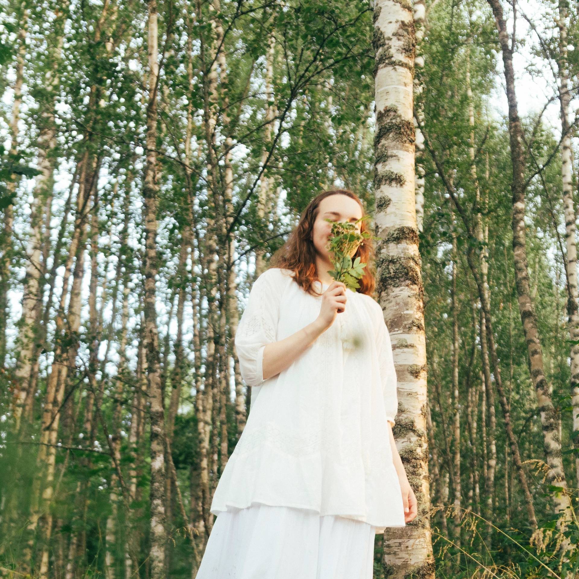 A girl smelling a budle of flowers in a birch forest.