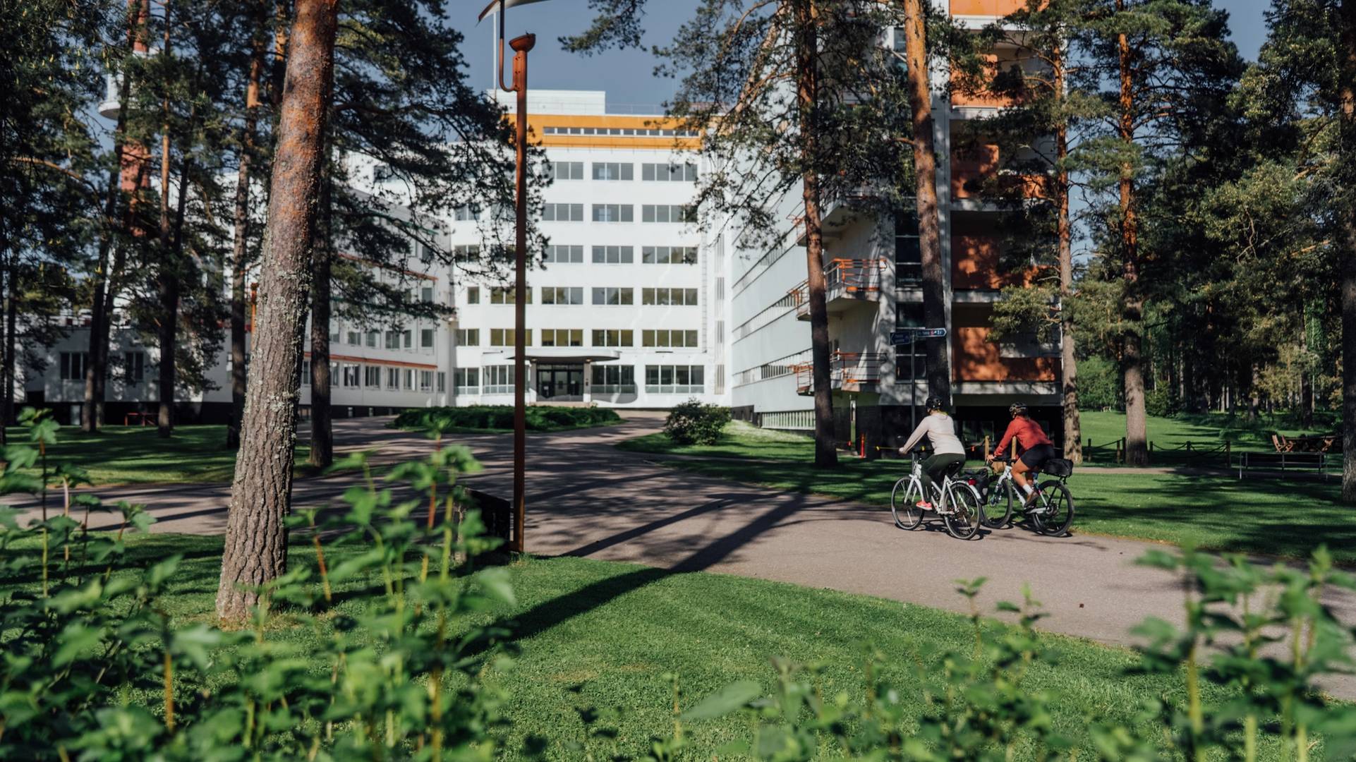 A couple biking through the pine forest towards Paimio Sanatorium