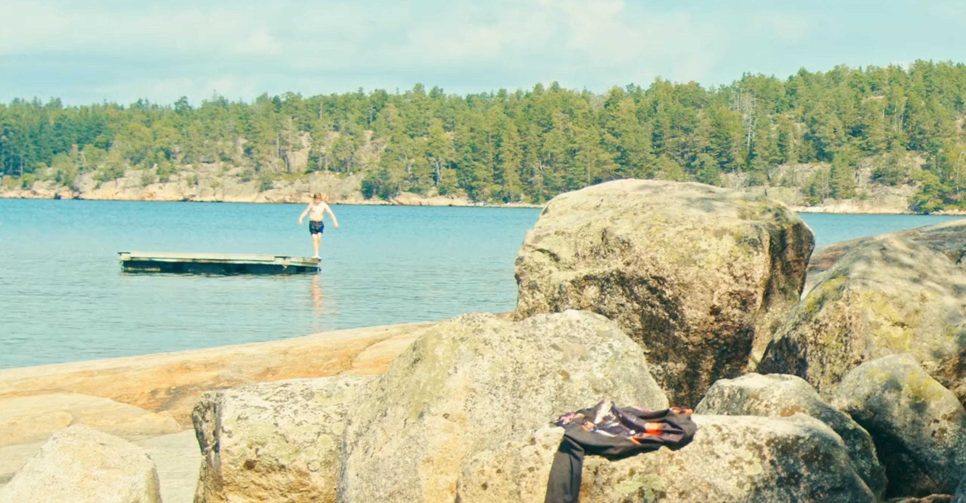 A rocky beach, with a person standing on a swimming dock.
