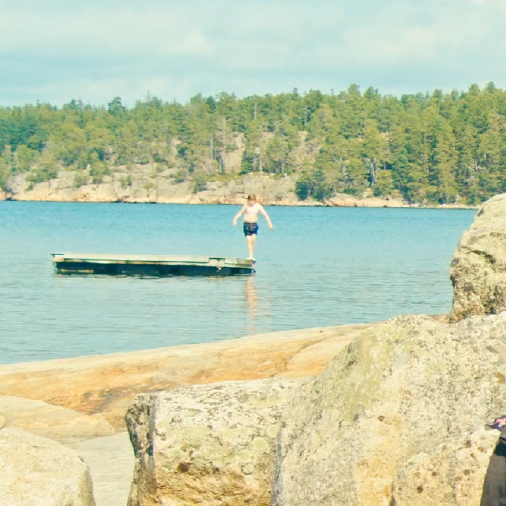 A rocky beach, with a person standing on a swimming dock.