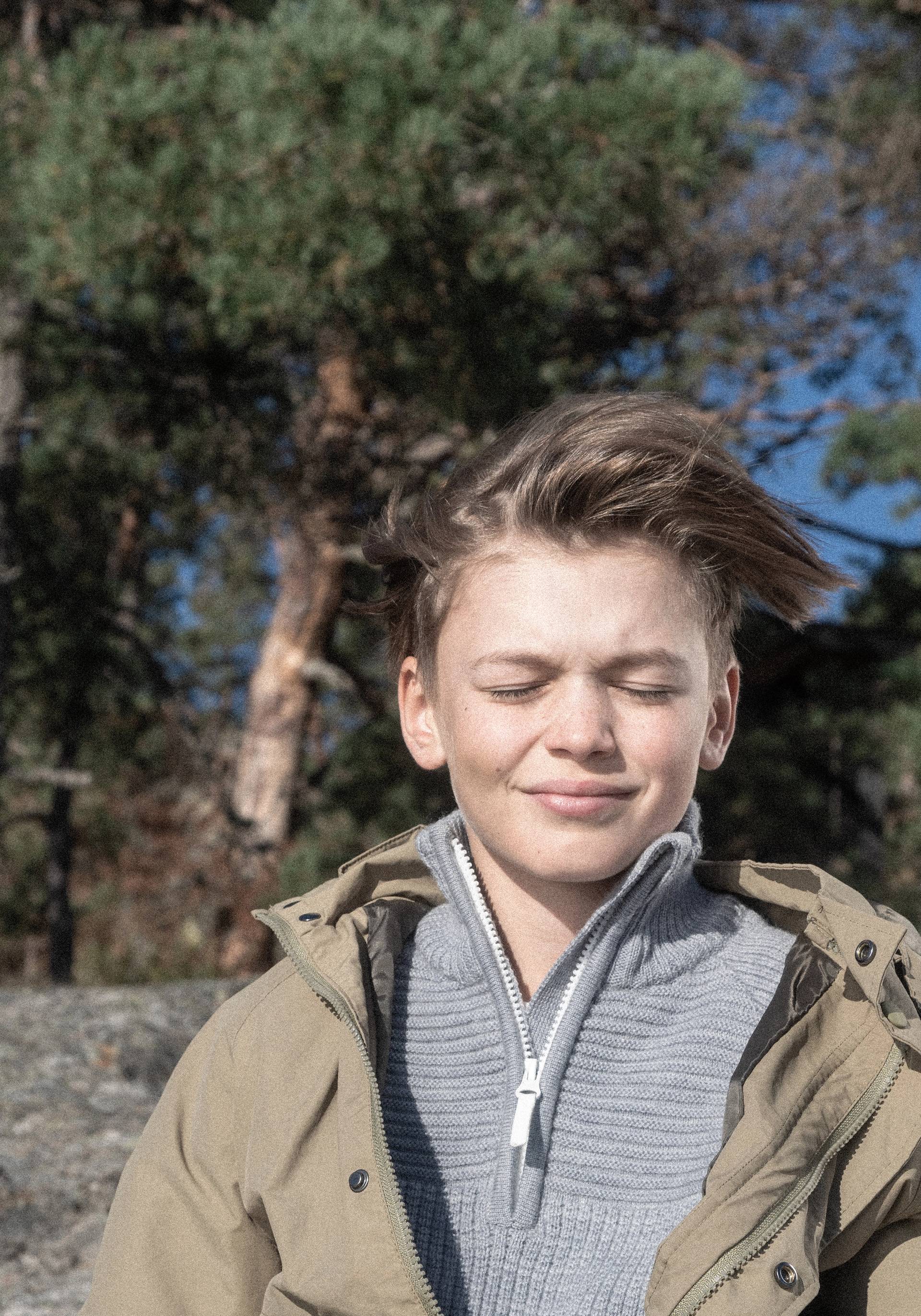A boy enjoying the sun with his eyes closed.