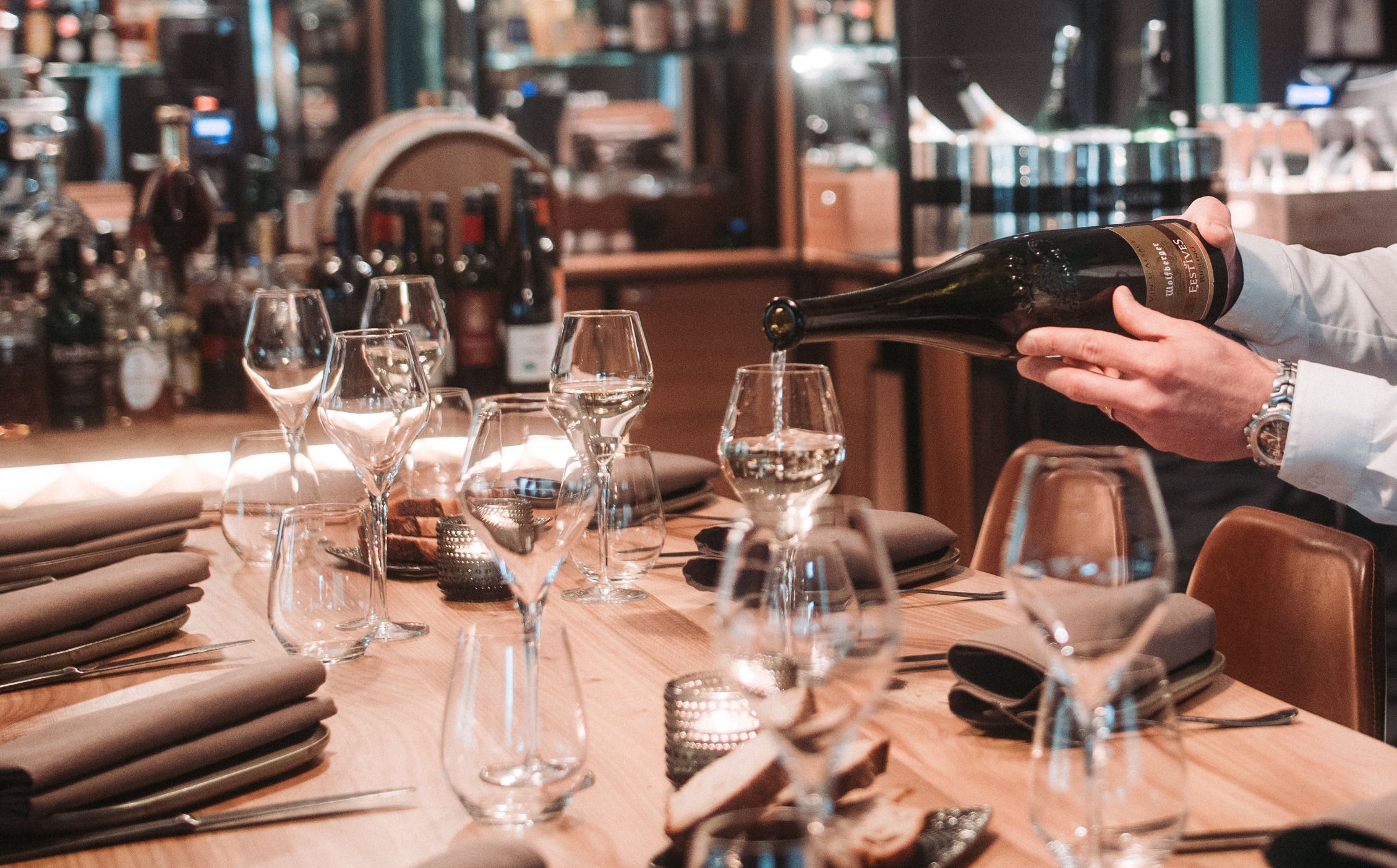 A table setting with a person pouring wine.