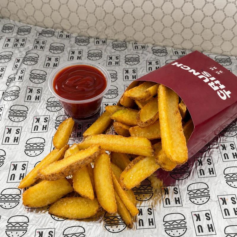 Skin-on rustic fries spilling out of a red Husk box, with a cup of ketchup
