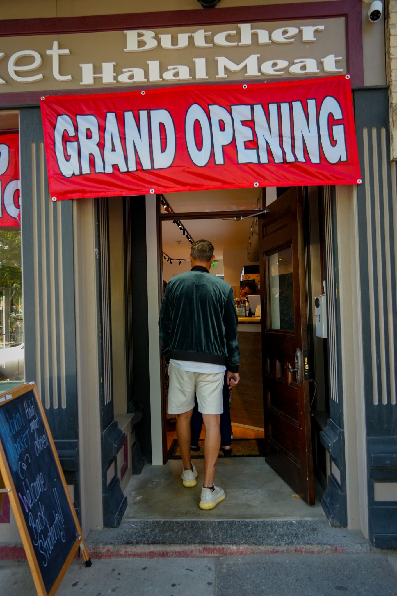 Grand opening banner at halal butcher storefront with customer entering