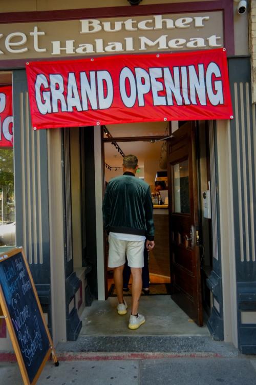 Grand opening banner at halal butcher storefront with customer entering