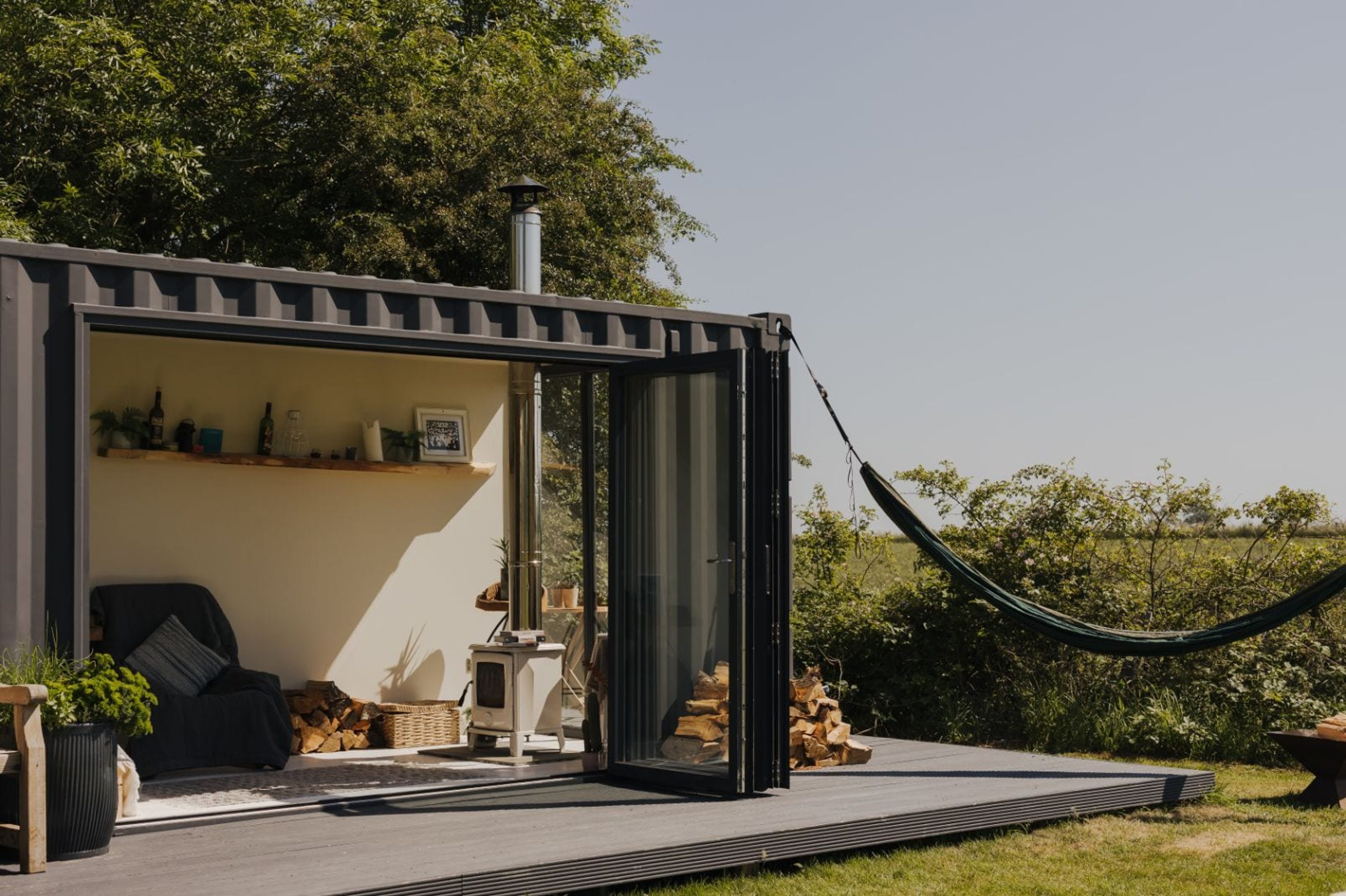 A modern container cabin with bifold doors open onto a deck and countryside