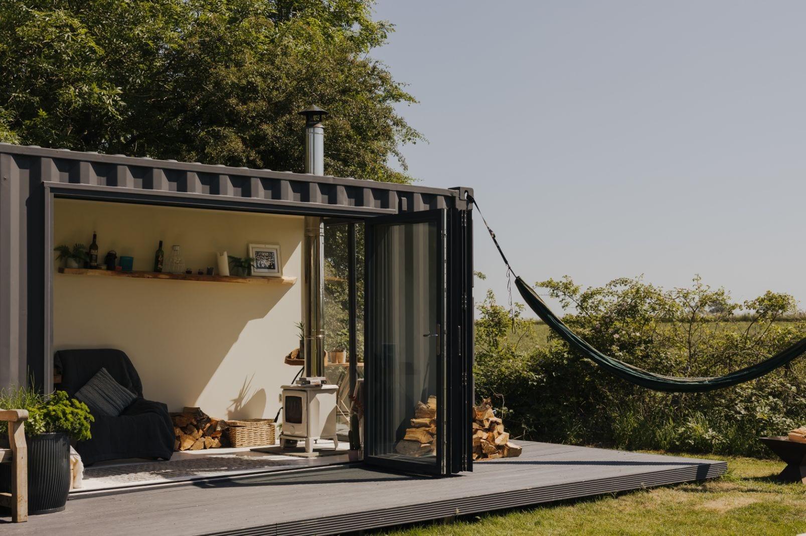 A modern container cabin with bifold doors open onto a deck and countryside