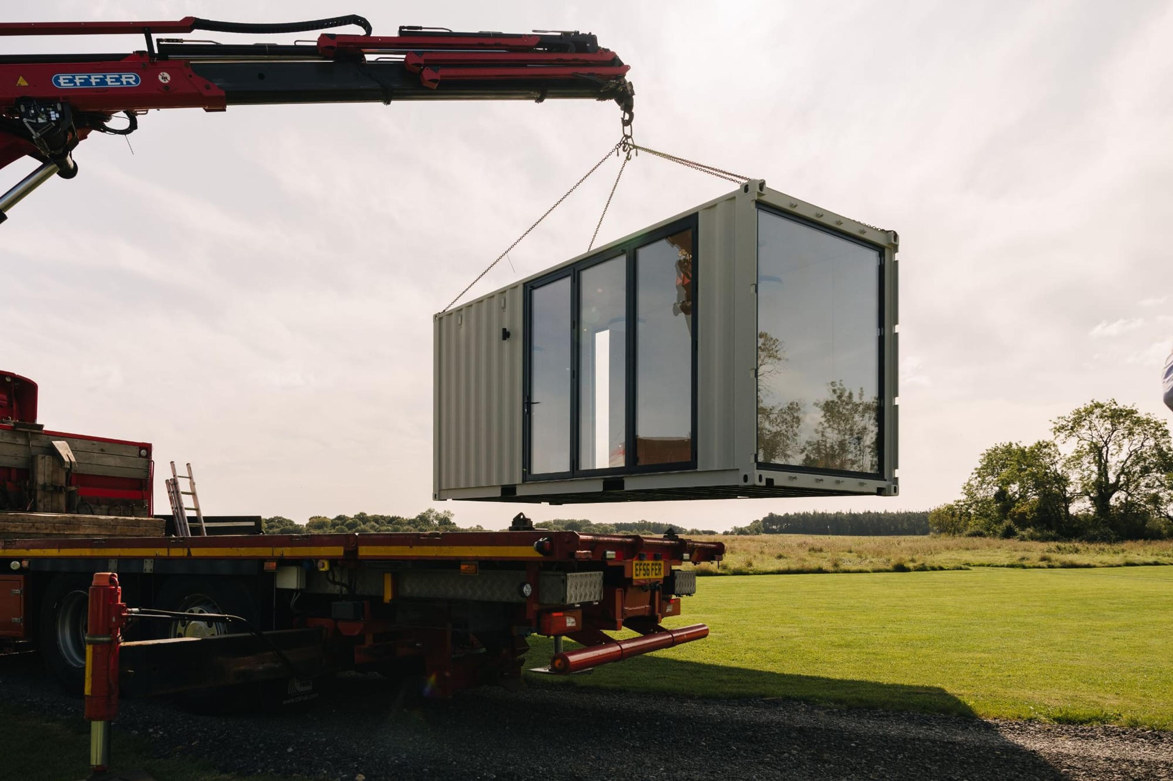 A crane lifting a glazed modular container building onto site