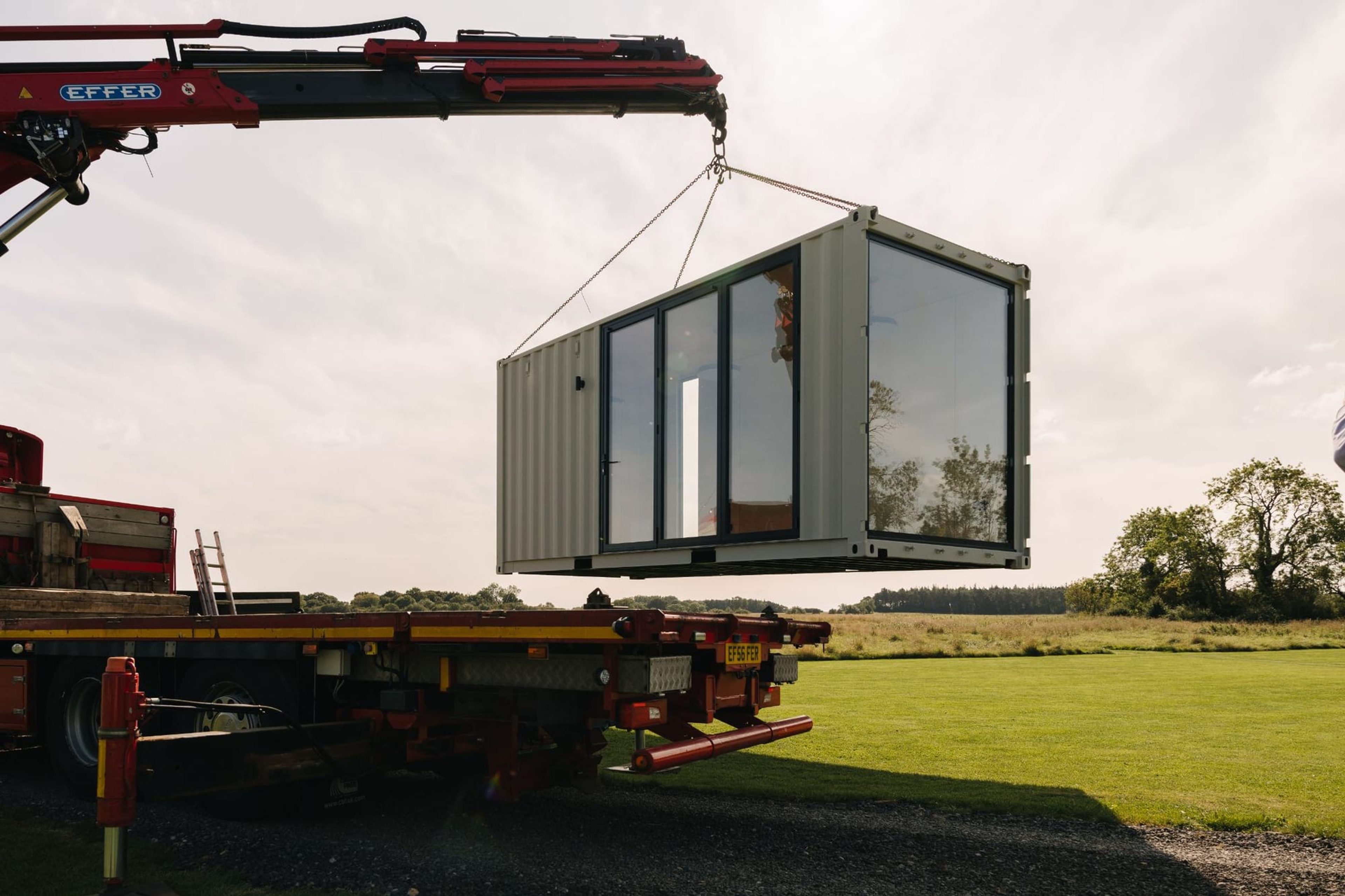 A crane lifting a glazed modular container building onto site