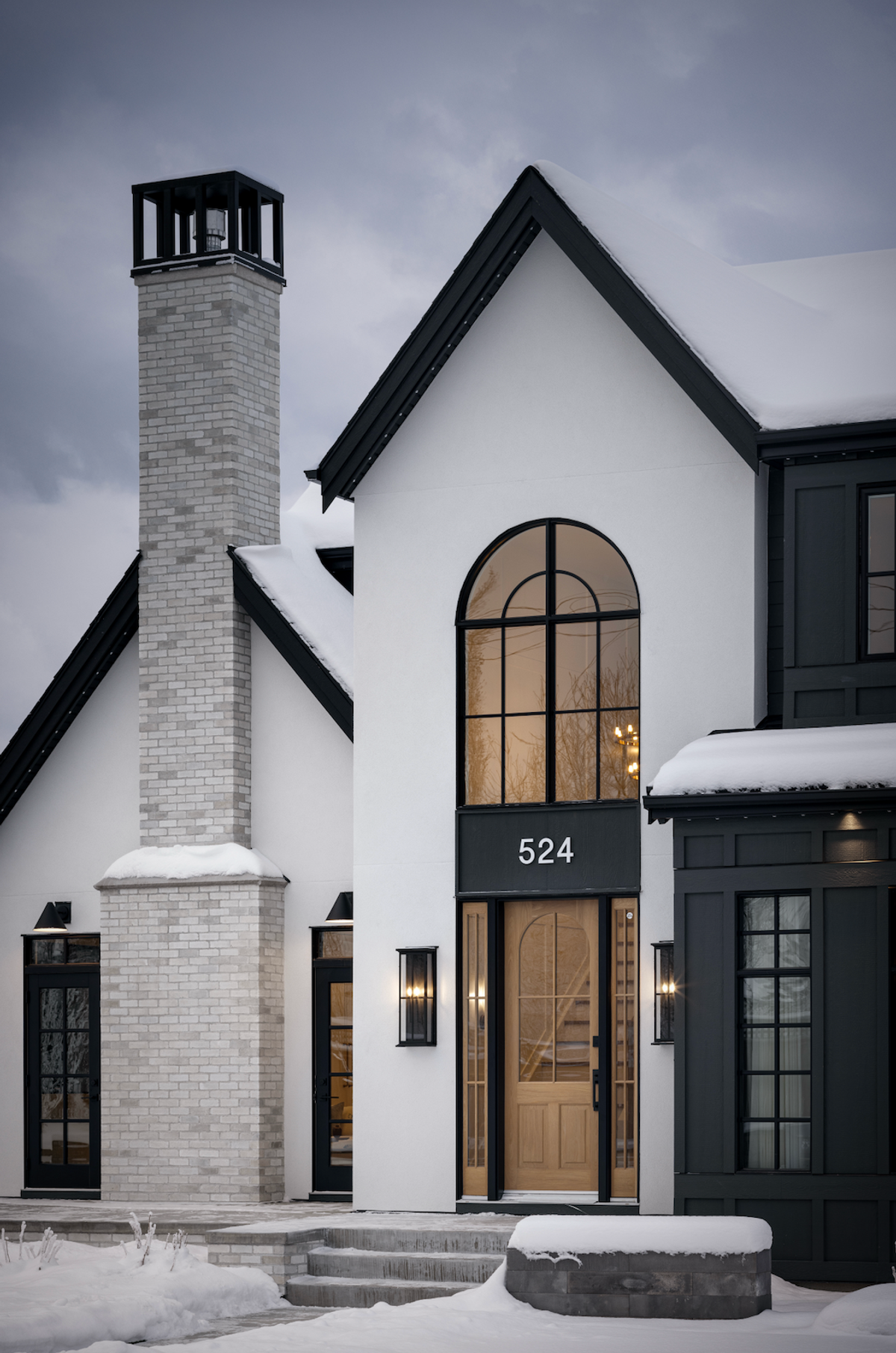 Snow-covered home with arched window and brick chimney