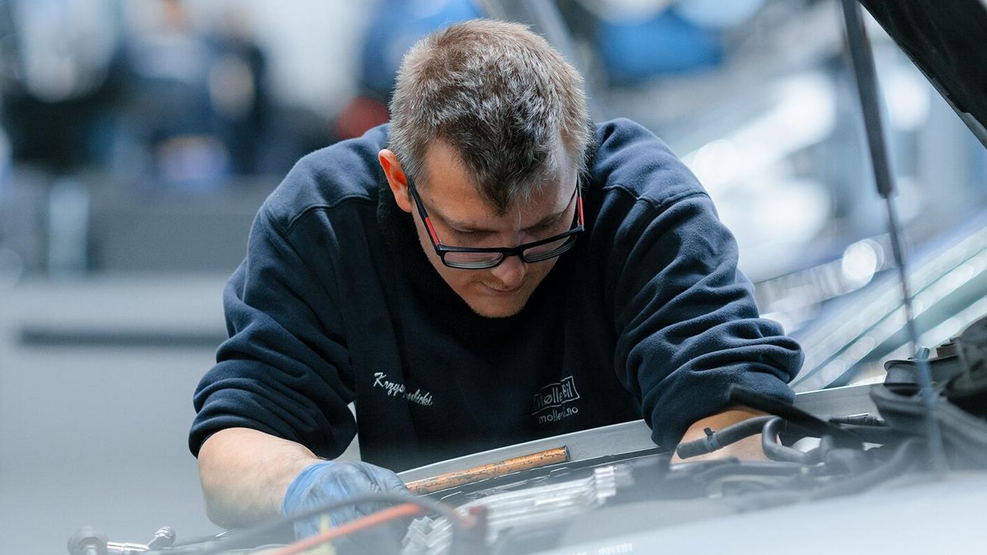 En Møller Bil ansatt fra verkstedet som jobber på en bil. Kikker ned i motorrom