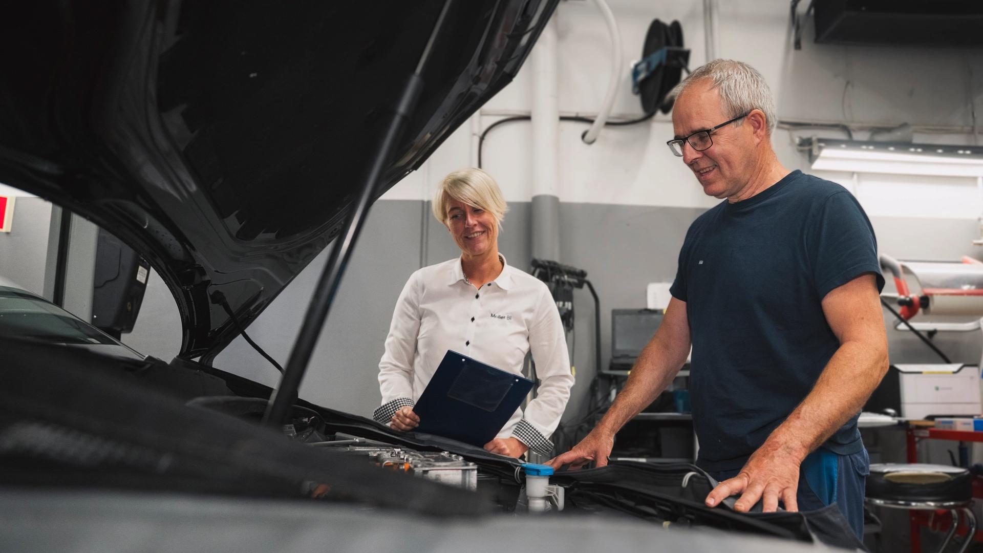 Serviceleder og mekaniker som ser ned i motorrommet på en bil