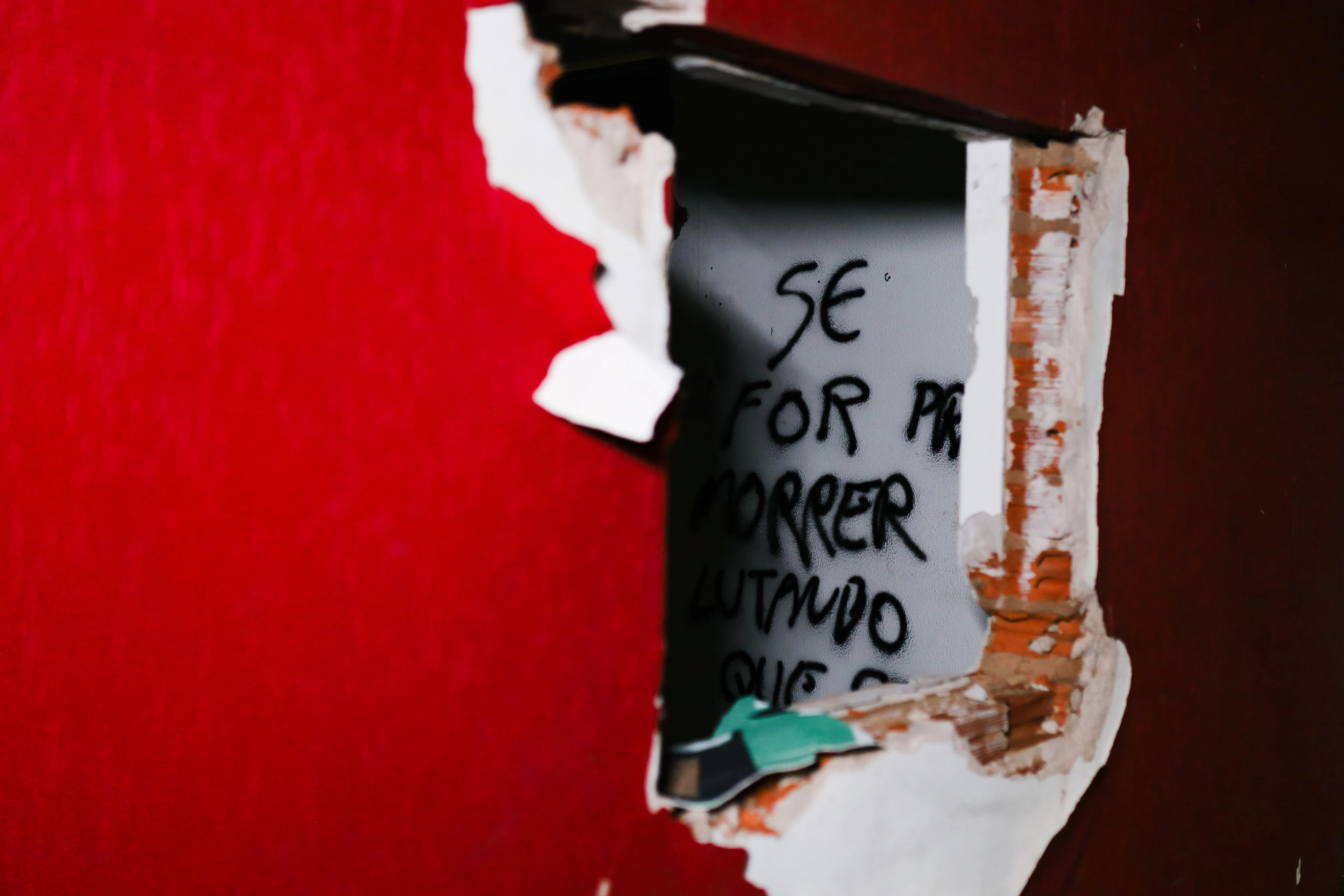 Cartaz rasgado sobre parede vermelha com frase escrita à mão