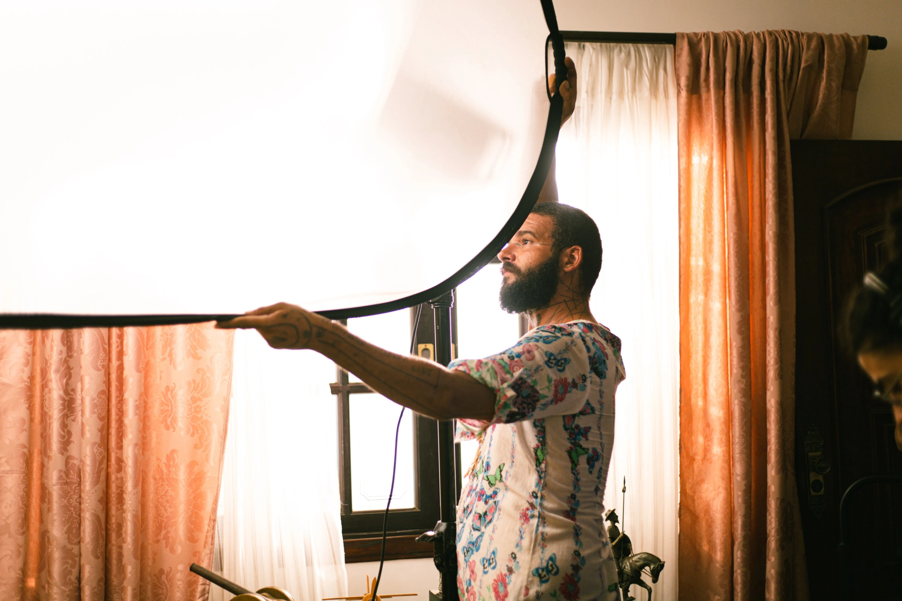 Técnico ajustando um rebatedor grande junto à janela, num set de filmagem