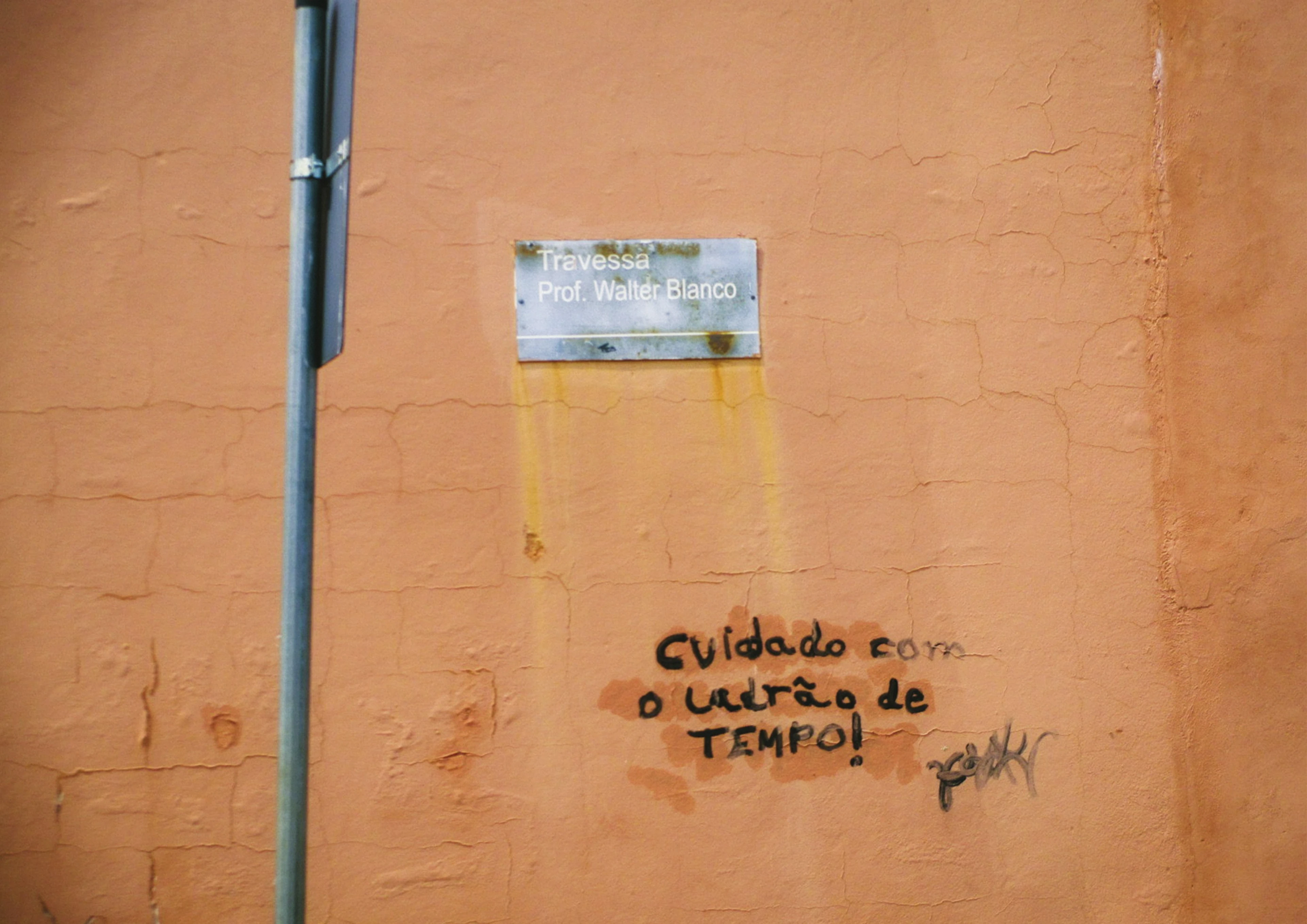 Parede laranja com a frase “Cuidado com o ladrão de tempo!” embaixo de uma placa de rua