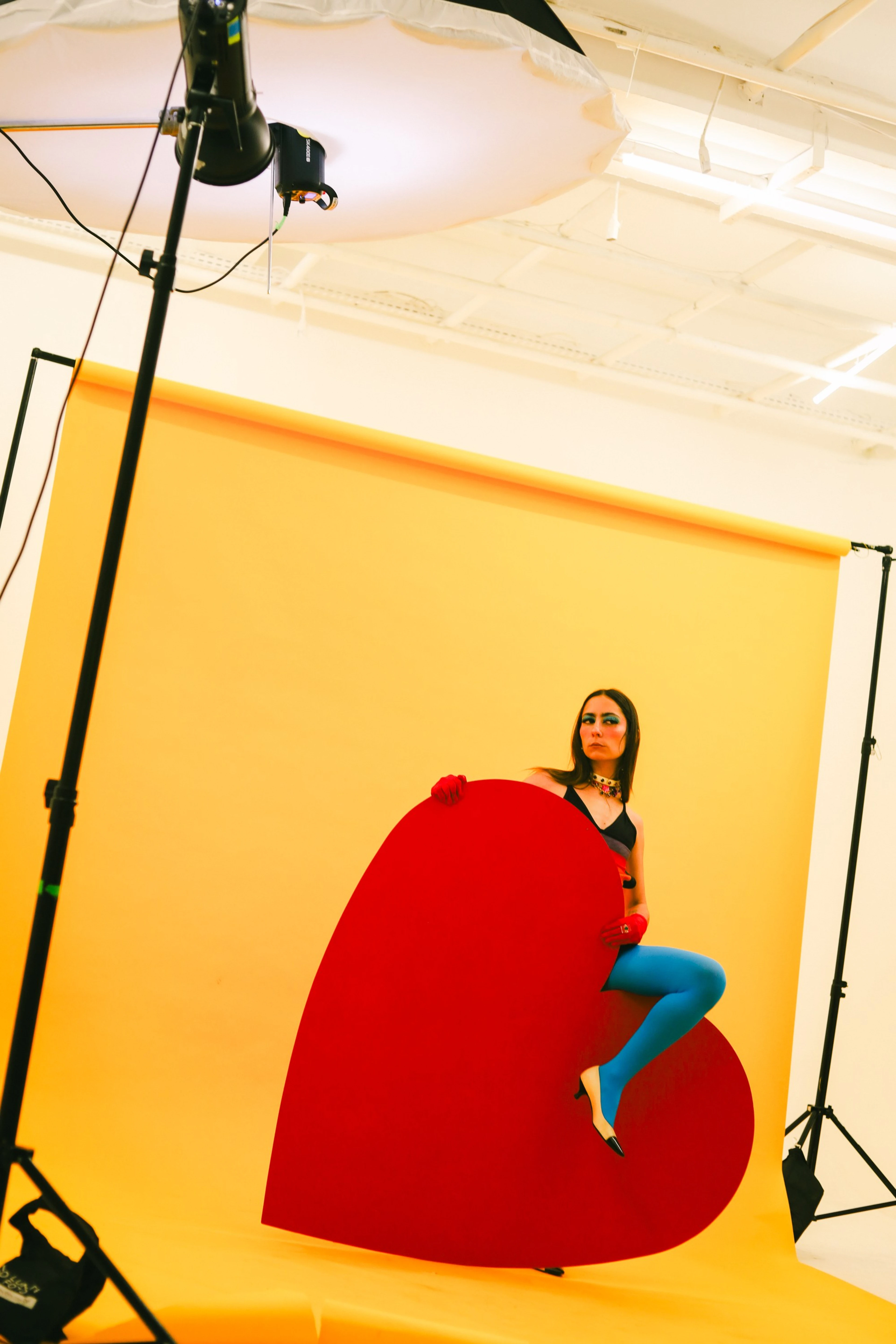 Modelo sentada sobre um grande coração vermelho num estúdio de fundo amarelo