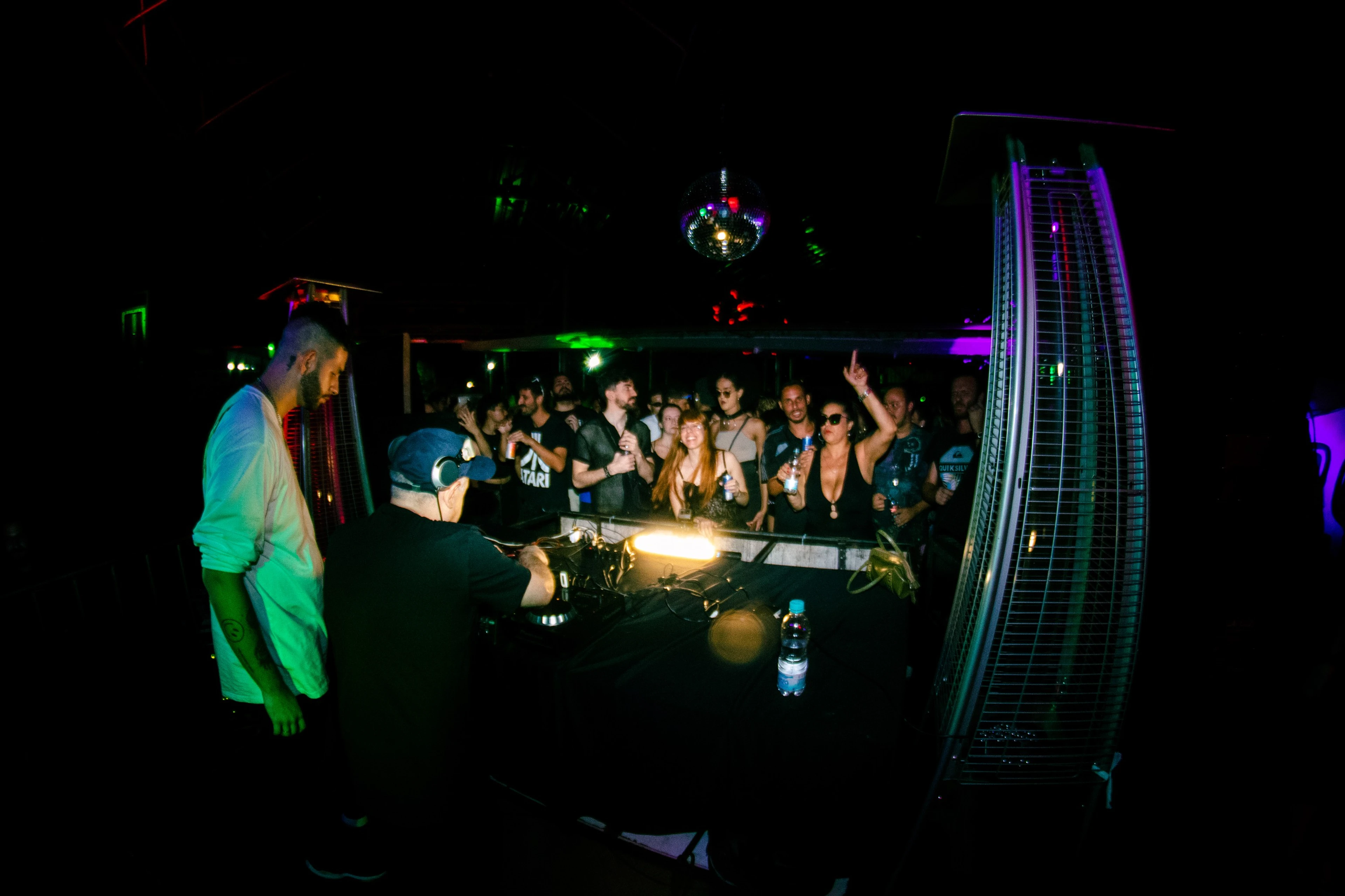Público em volta da cabine do DJ numa festa, vista com lente olho de peixe
