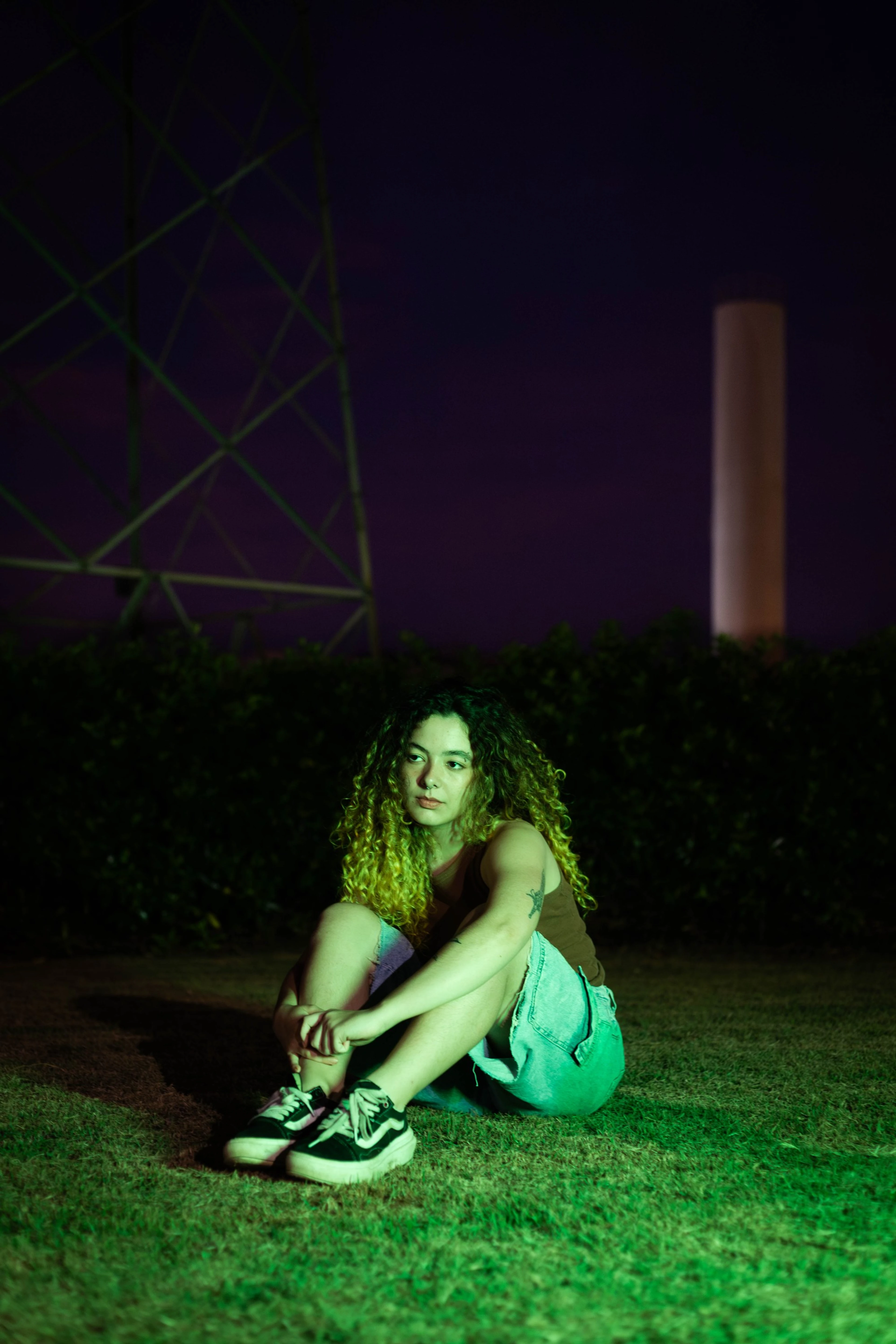 Mulher sentada na grama à noite, iluminada por luz verde