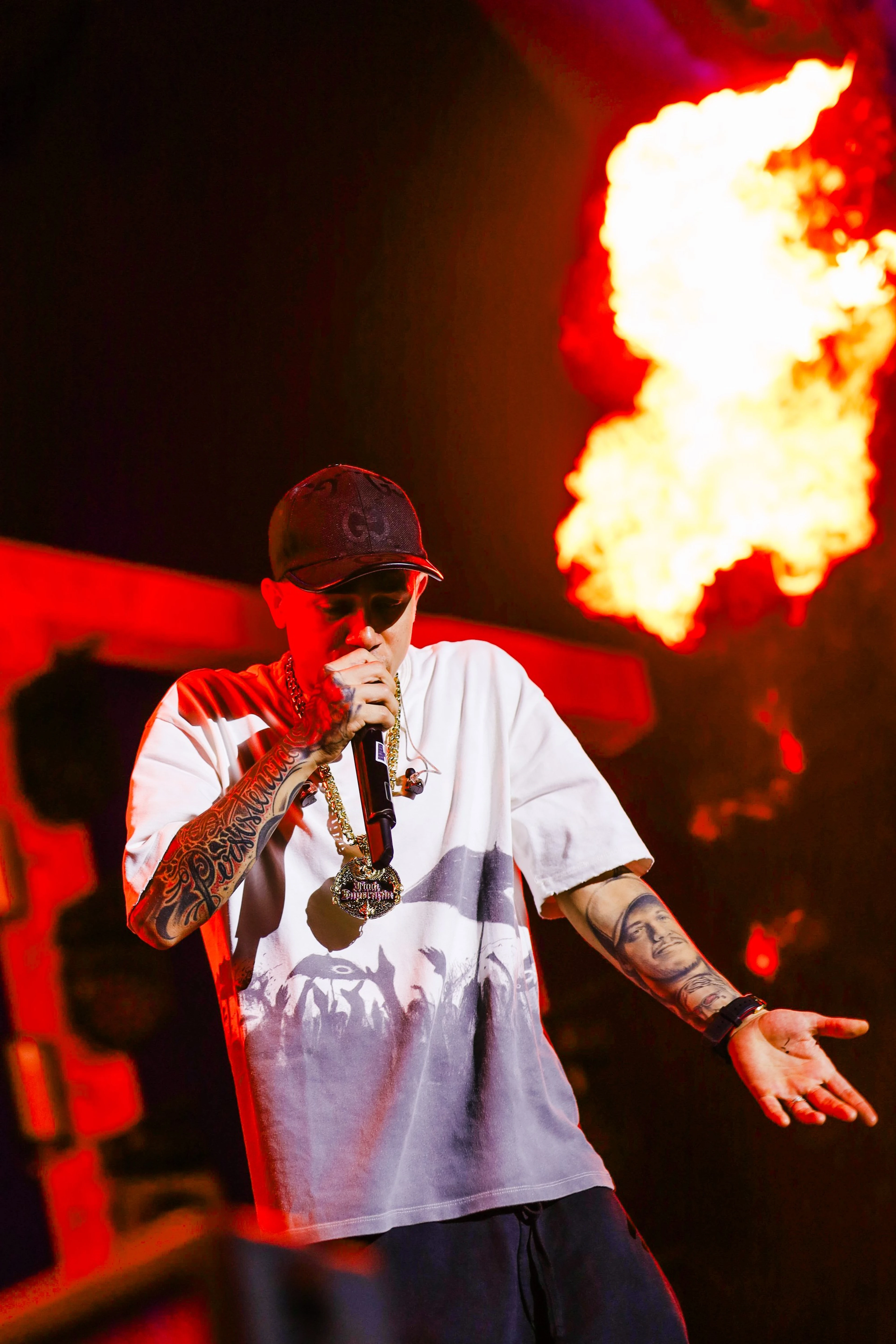Rapper de boné e camiseta branca cantando, com uma labareda ao fundo