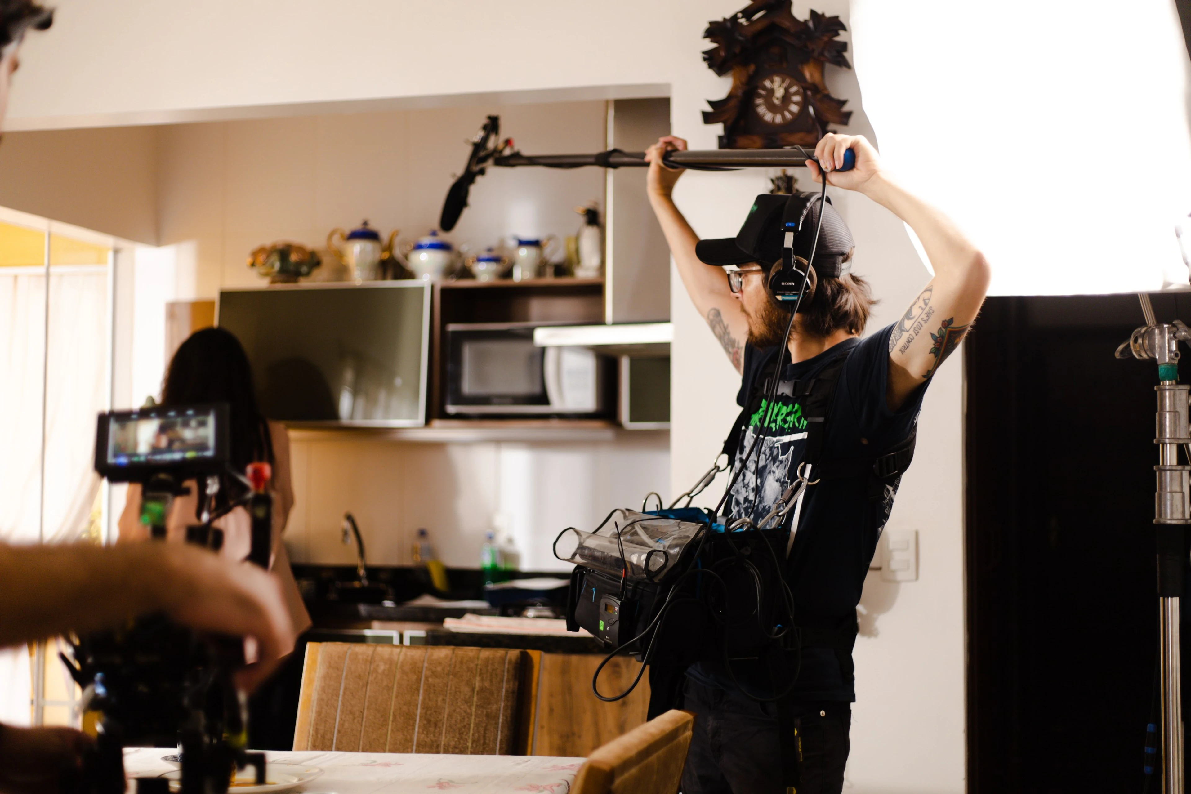 Equipe filmando numa cozinha, com o microfone boom erguido embaixo de um relógio cuco