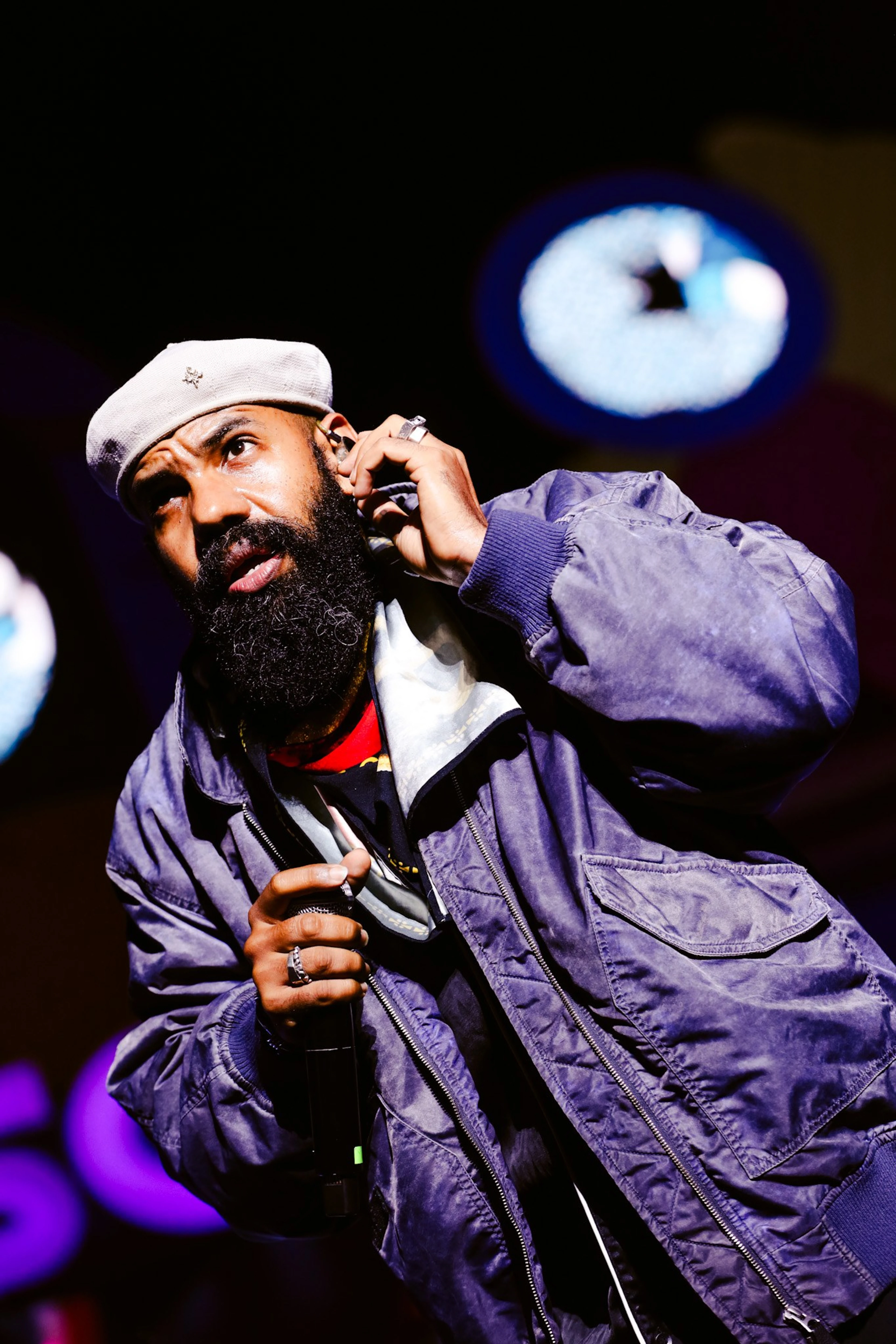 Rapper de barba e boina branca segurando o microfone no palco