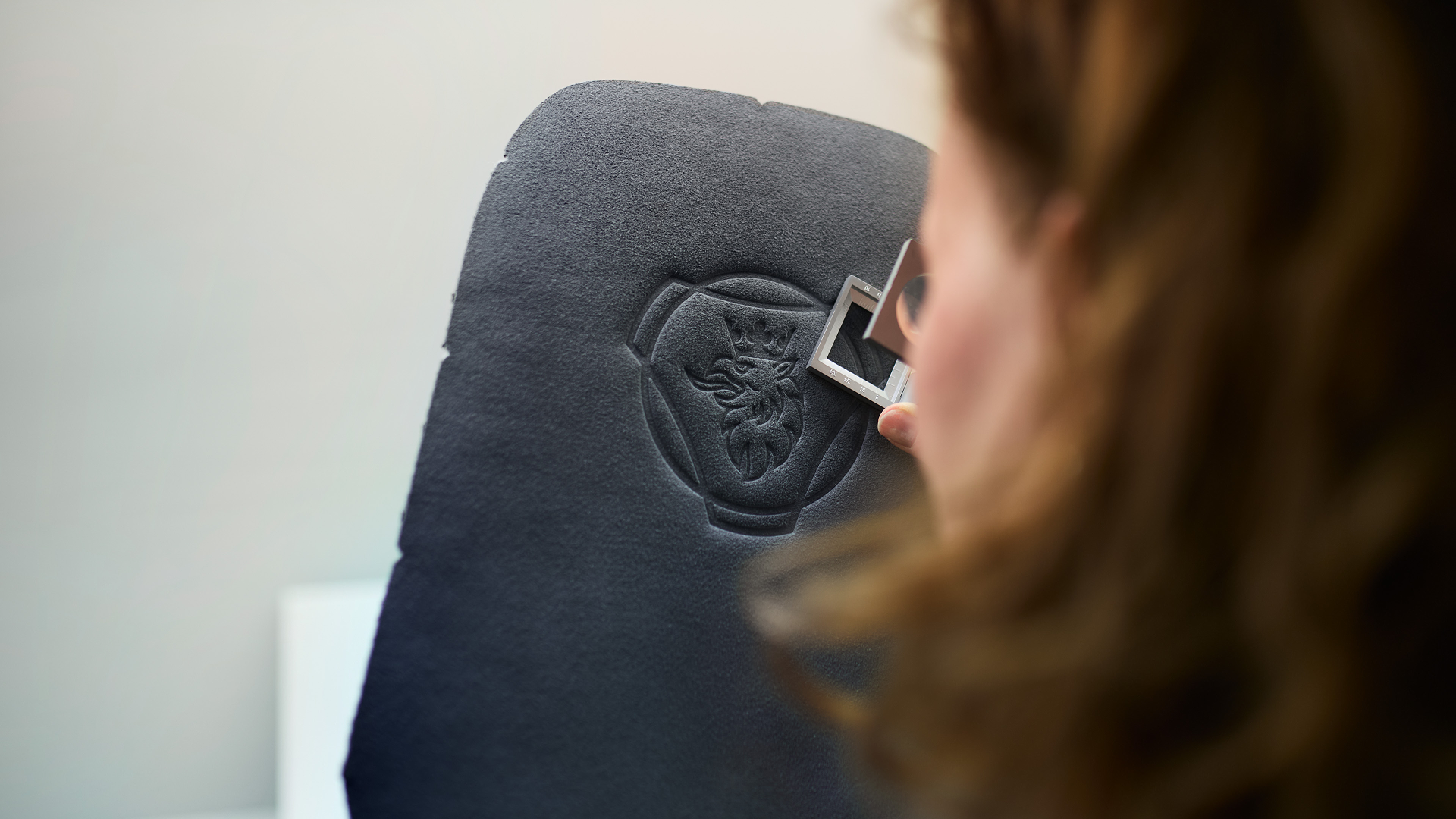 Person inspecting a black material panel embossed with the Scania griffin logo, using a small measuring tool for precision.