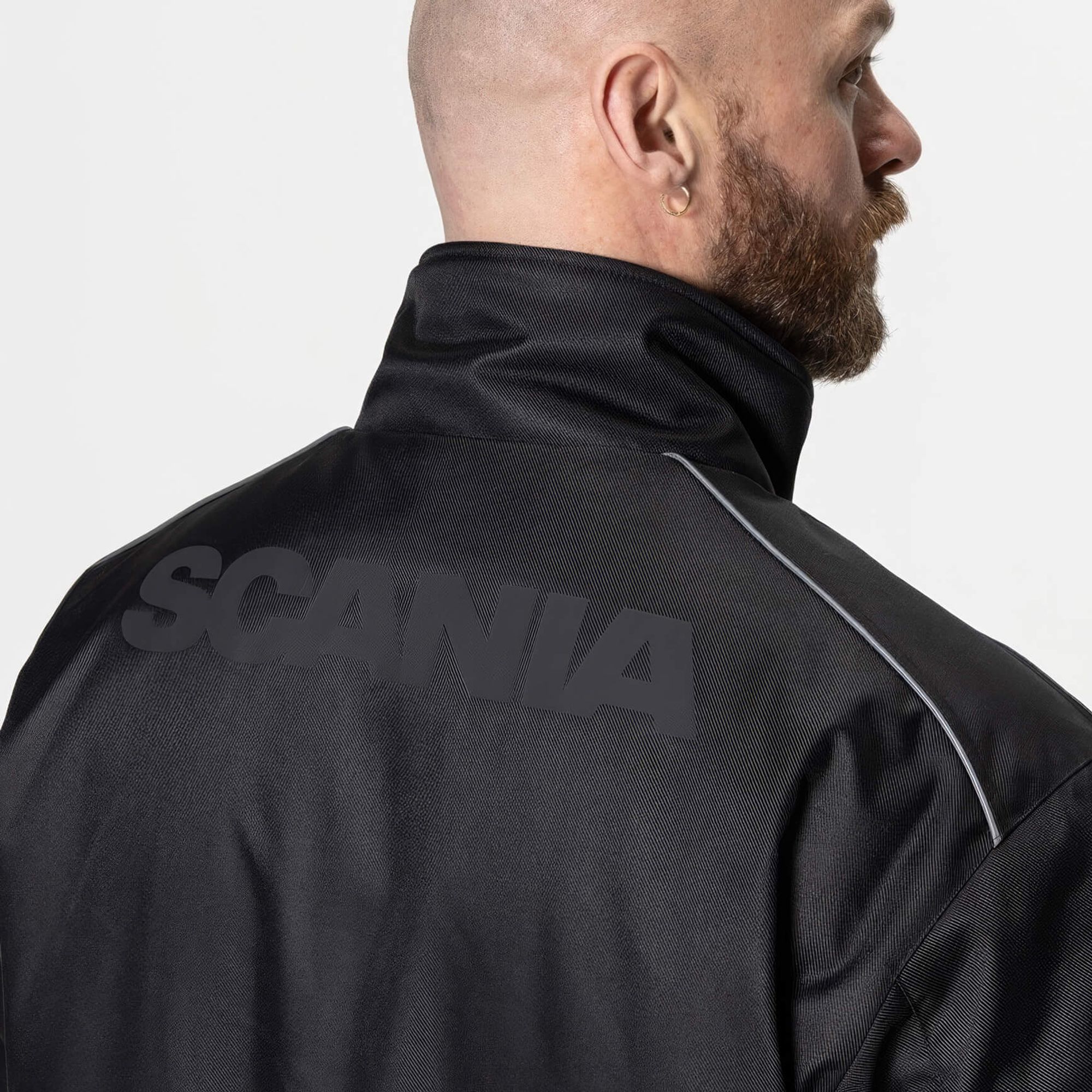 Man wearing black jacket with black Scania logotype on the back.