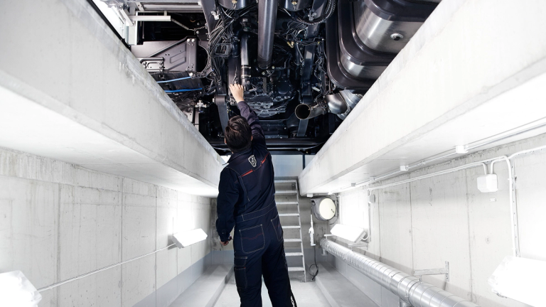 Mechanic working underneath a Scania truck in a brightly lit service bay.