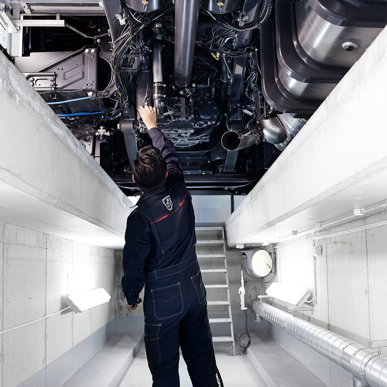 Mechanic working underneath a Scania truck in a brightly lit service bay.