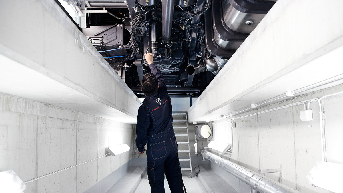 Mechanic working underneath a Scania truck in a brightly lit service bay.