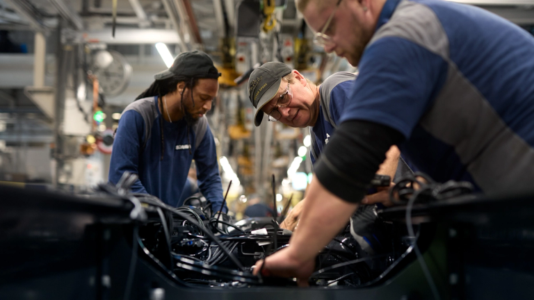 Three Scania workers assembling machinery and wiring on the factory floor.