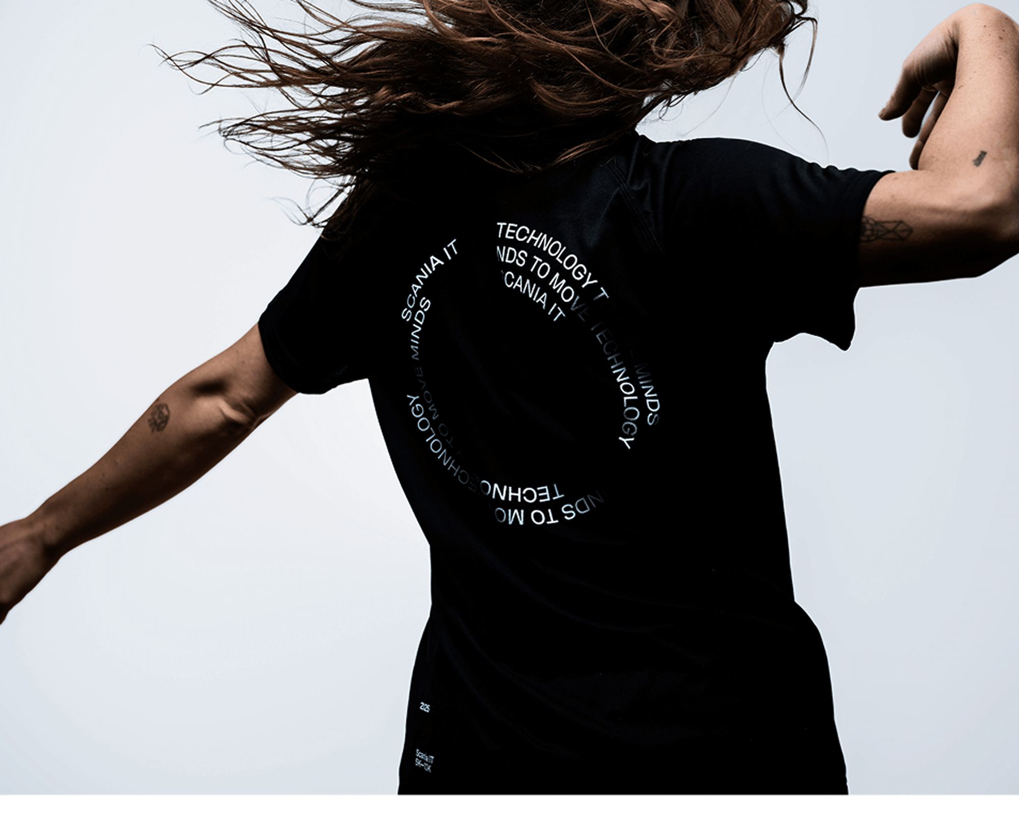 Woman with long hair in motion wearing a black t-shirt with circular white text on the back.