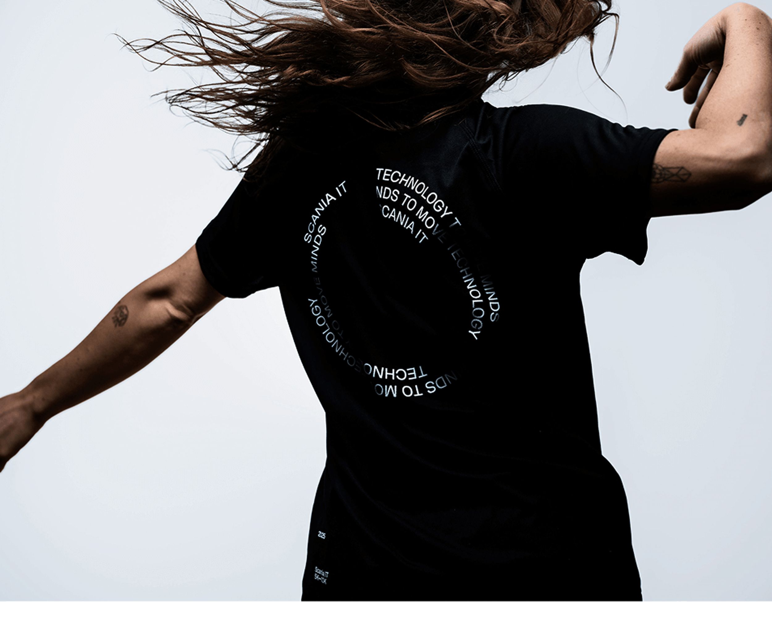 Woman with long hair in motion wearing a black t-shirt with circular white text on the back.
