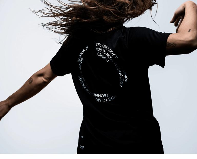 Woman with long hair in motion wearing a black t-shirt with circular white text on the back.