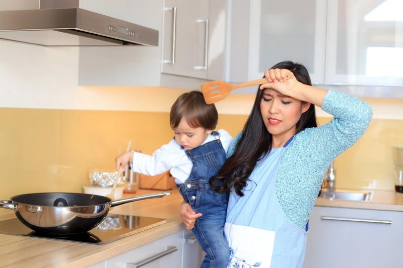 Ibu menggendong anak sambil memasak di dapur, menggambarkan kesibukan harian saat menyiapkan lauk MPASI