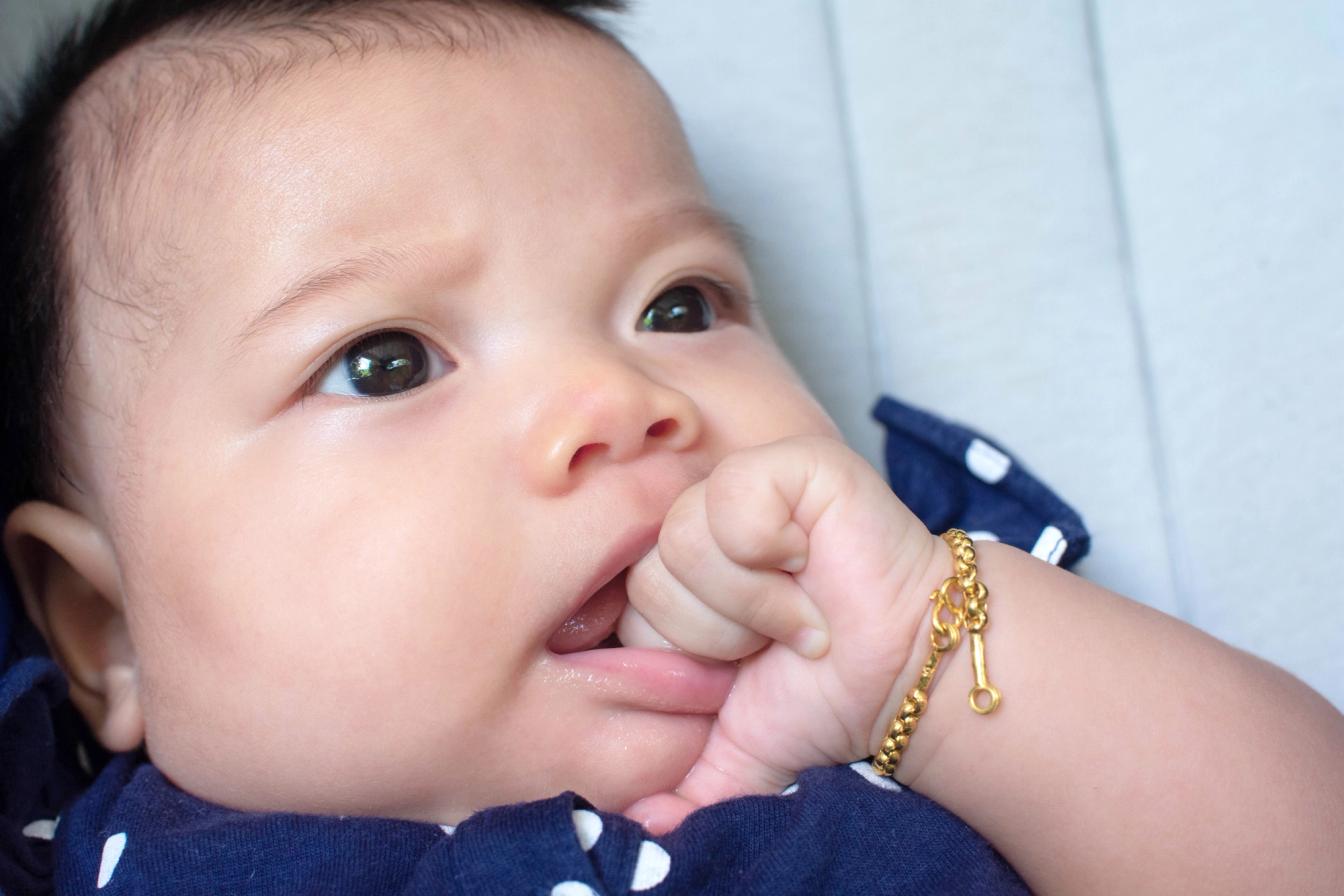Bayi memegang tangan dekat mulut, menggambarkan kehati-hatian memilih makanan yang aman untuk anak