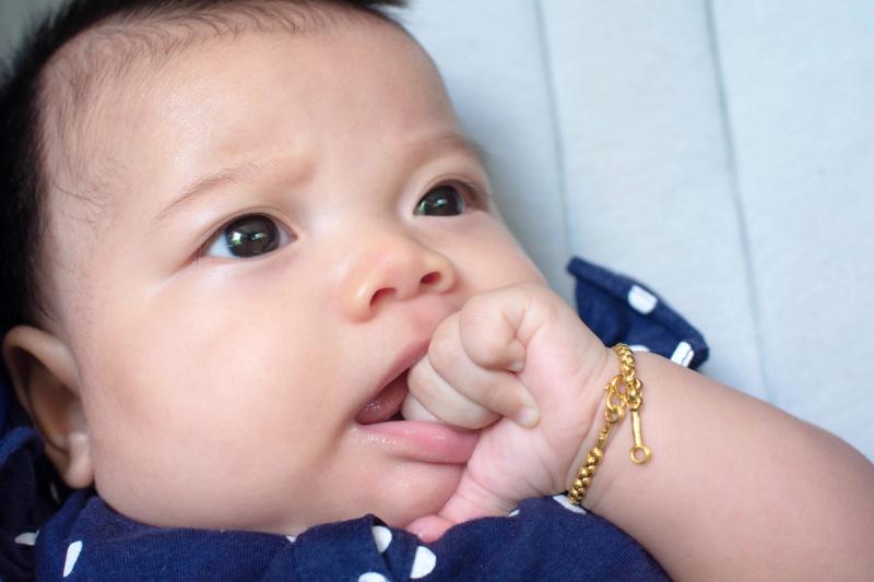 Bayi memegang tangan dekat mulut, menggambarkan kehati-hatian memilih makanan yang aman untuk anak