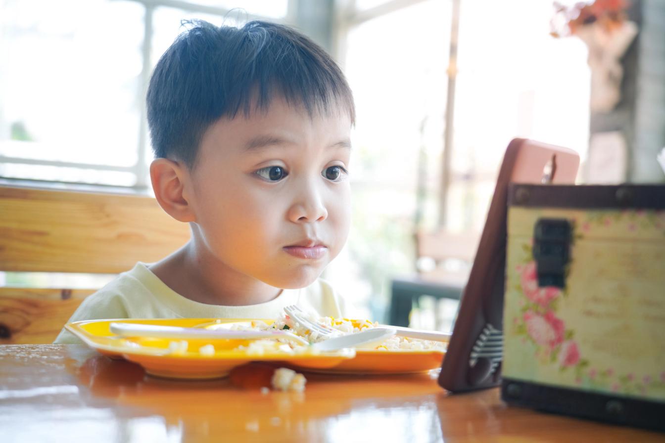 Anak laki-laki duduk di meja makan dengan piring berisi makanan di depannya