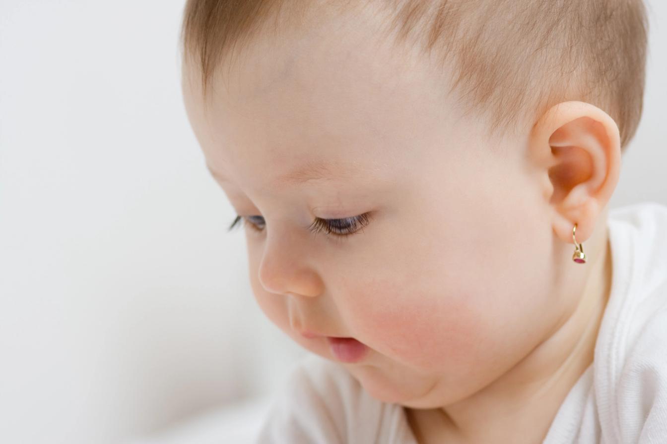 Close-up wajah bayi menunduk memakai anting, menggambarkan tahap MPASI bayi