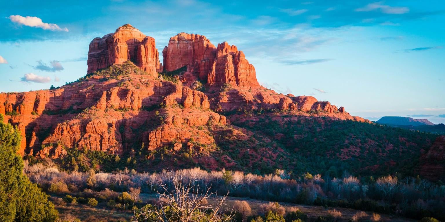Vibrant red rock formations and green trees under a blue sky.