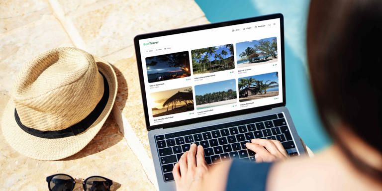 A person views tropical destinations on a laptop by a pool, next to a straw hat and sunglasses.