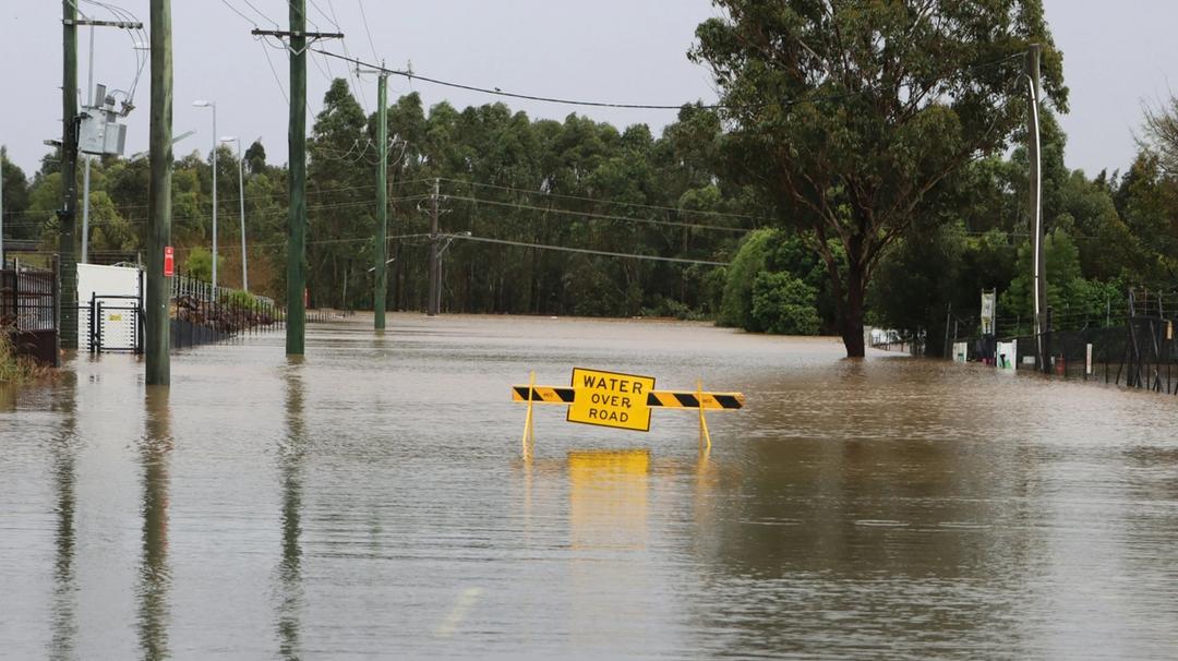 A flooded street with a yellow sign reading "water over road"