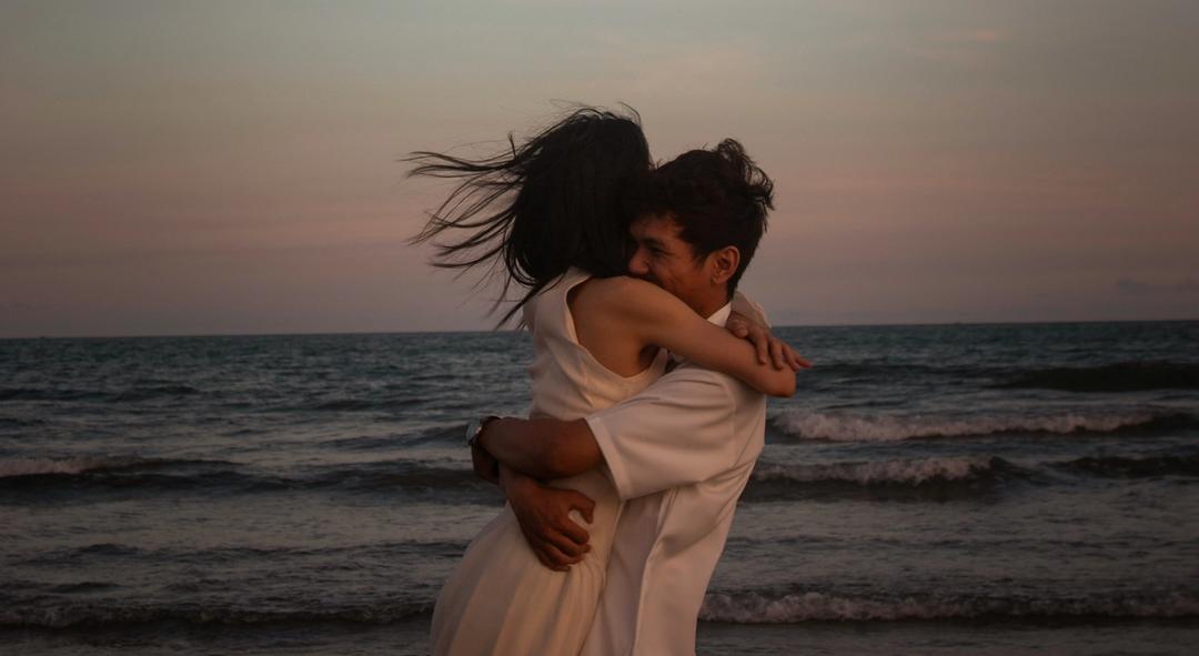 A man and woman hugging on the beach during sunset.