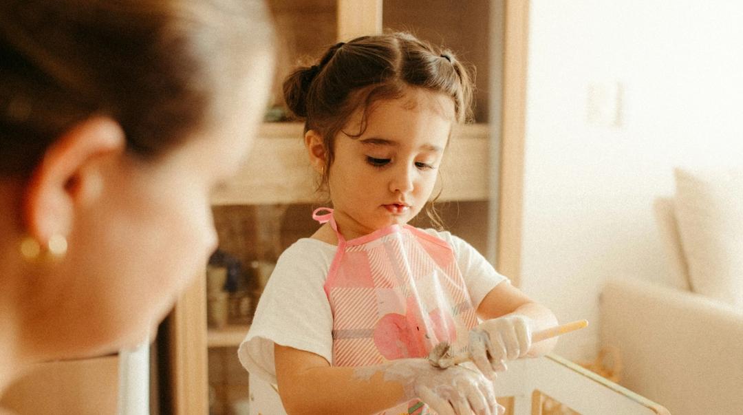 Child painting with adult watching.